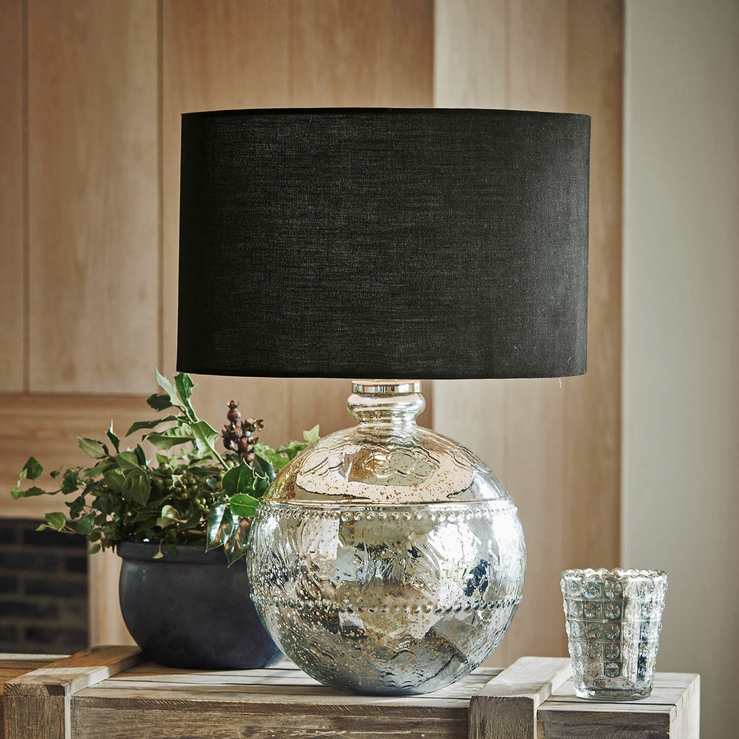 Dekorative Tischlampe mit silbernem Glasfuß und schwarzem Lampenschirm auf Holztisch