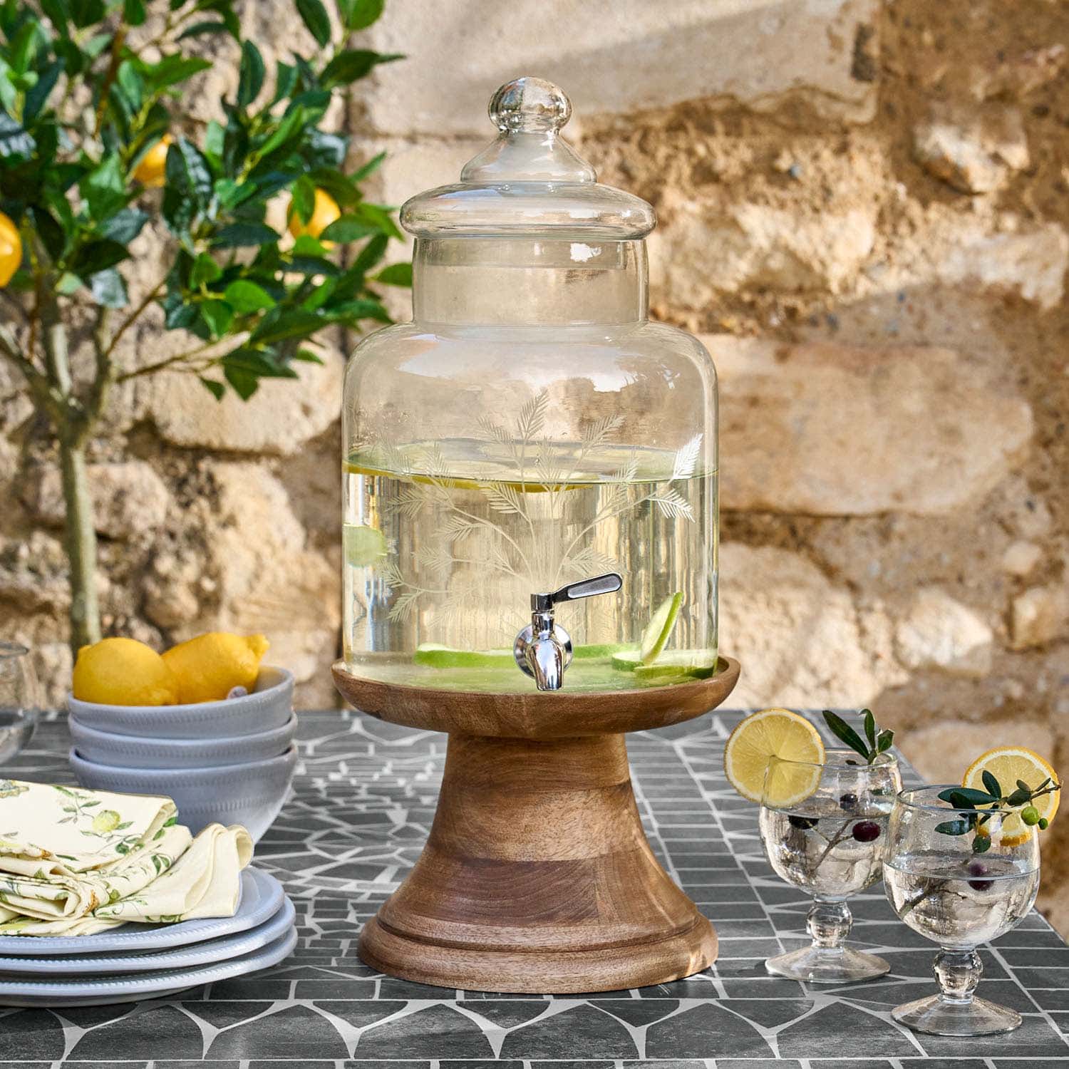 Glasgetränkespender mit Deckel auf Holzständer, gefüllt mit Wasser und Zitronenscheiben