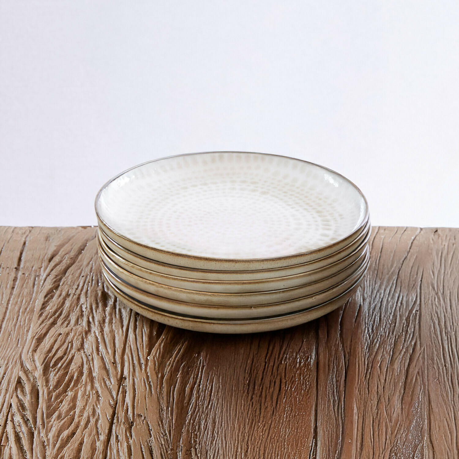 Set aus sechs weißen Keramiktellern mit feinem Muster und braunem Rand auf Holztisch