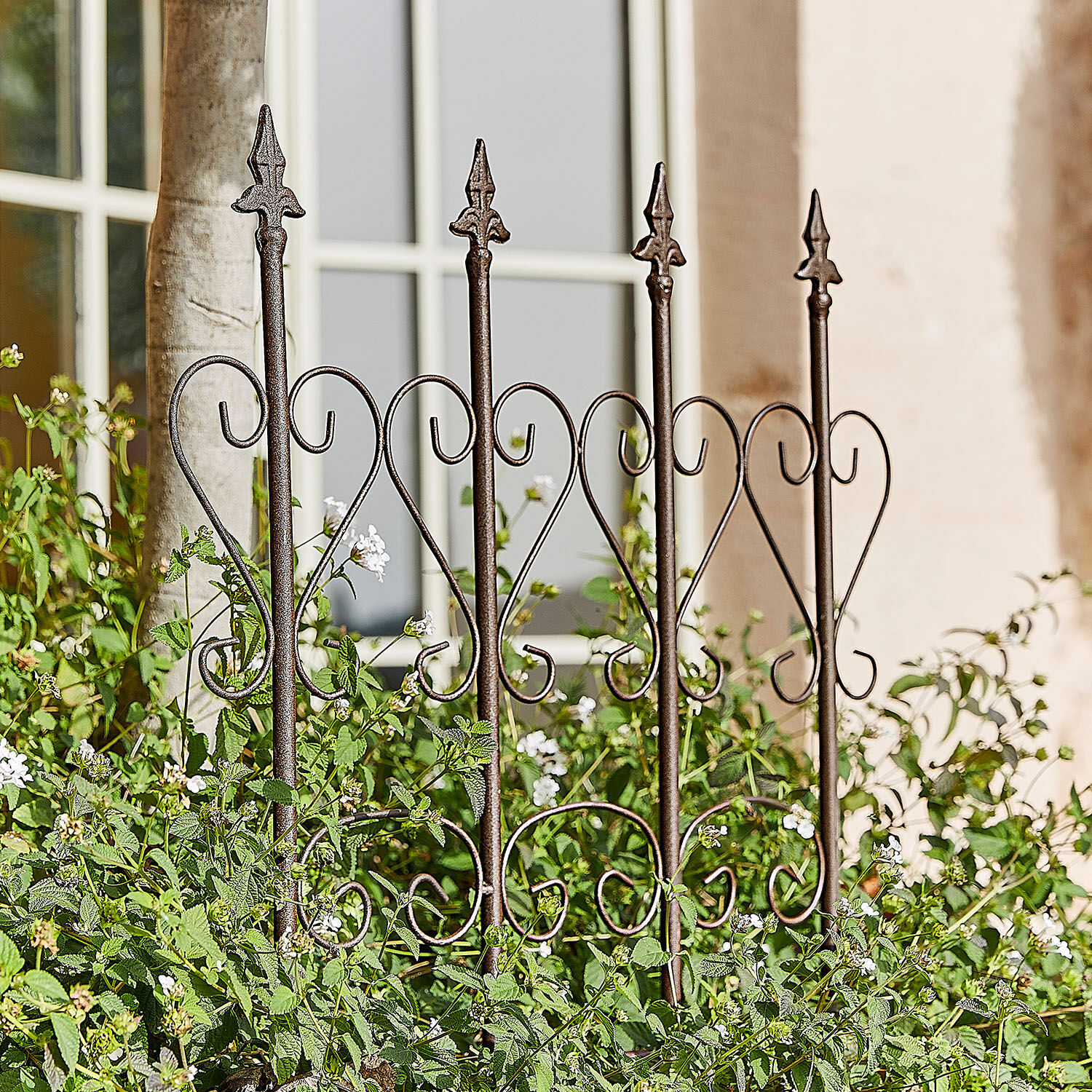Rankhilfe Nectarise Dekorativer Gartenzaun aus rostbraunem Metall mit Herzmotiv, umgeben von grünen Pflanzen und weißen Blüten
