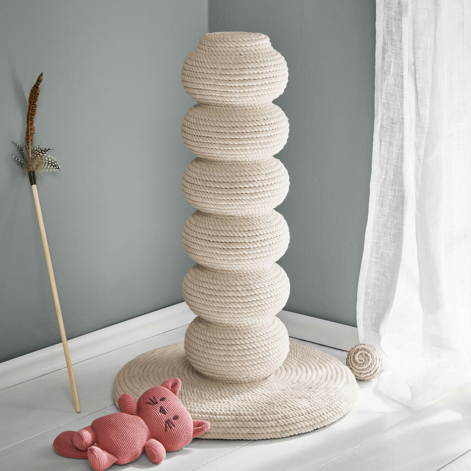 Katzenkratzbaum aus natürlichem cremefarbenem Seil mit Spielzeug und rosa Plüschkatze am Boden