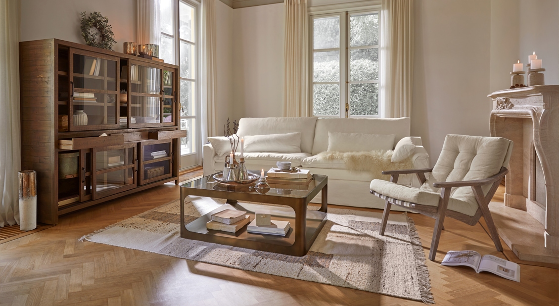 Gemütliches Wohnzimmer mit cremefarbenem Sofa, Holzsessel und Glastisch auf Teppich, natürliches Licht