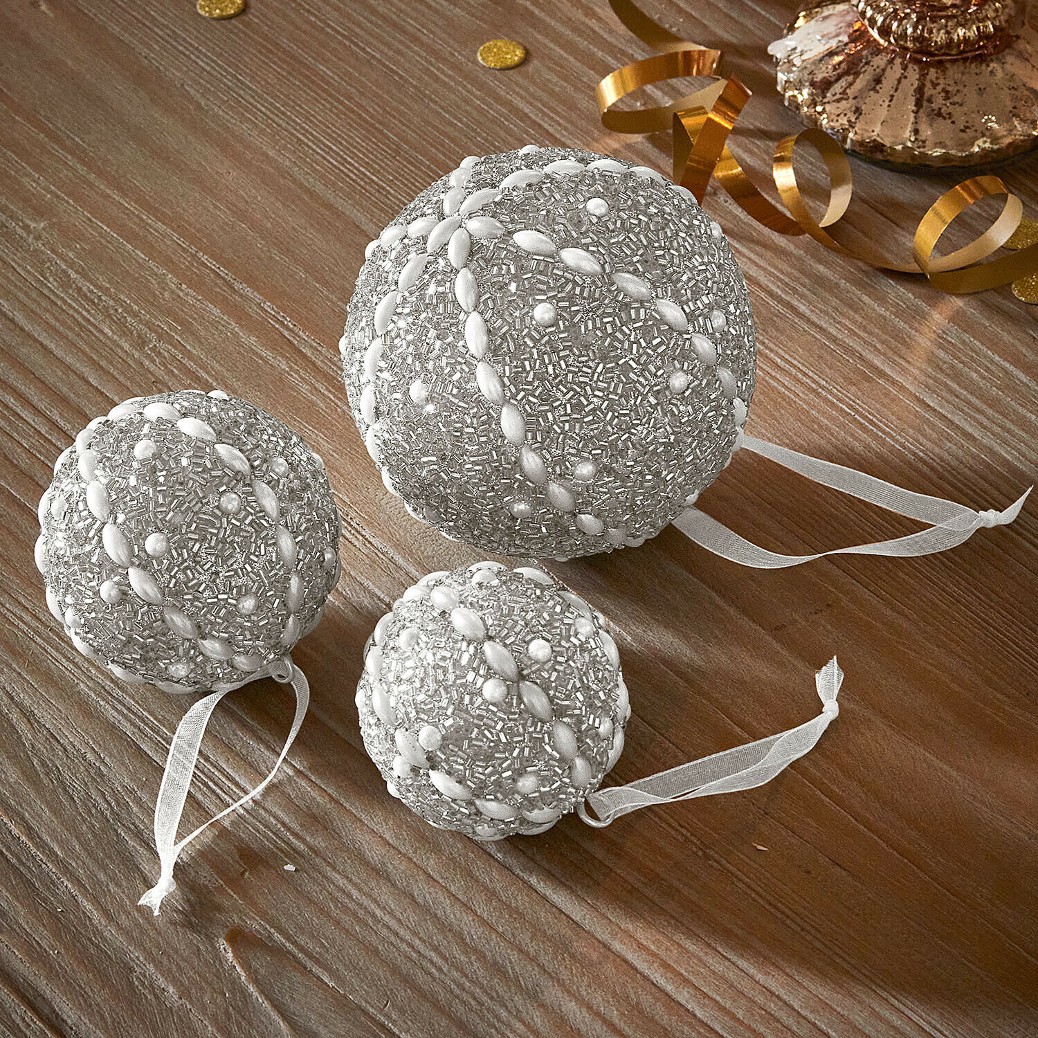 Weihnachtskugel 3er Set Maelvik Set aus drei silbernen Weihnachtskugeln mit Perlen und Bändern auf Holztisch