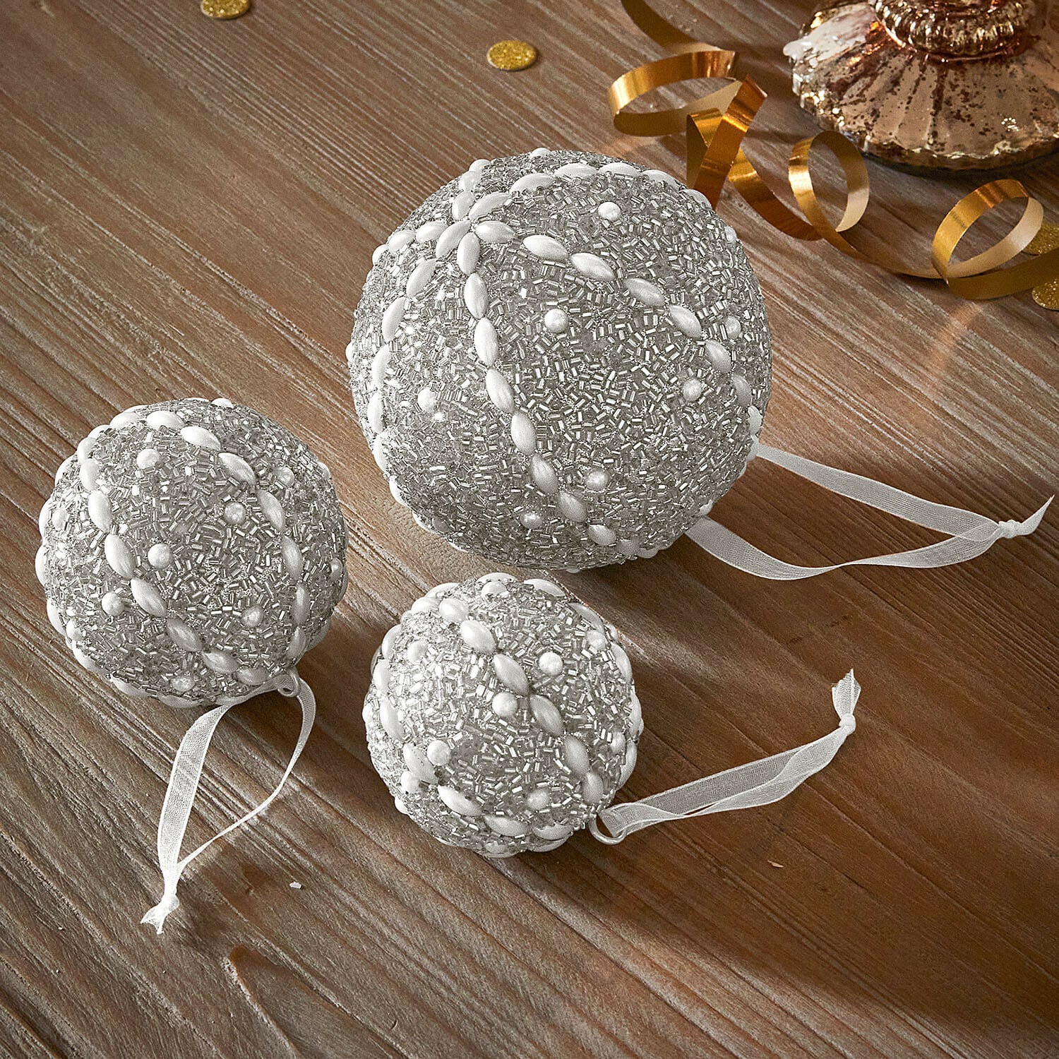 Weihnachtskugel 3er Set Maelvik Set aus drei silbernen Weihnachtskugeln mit Perlen und Bändern auf Holztisch