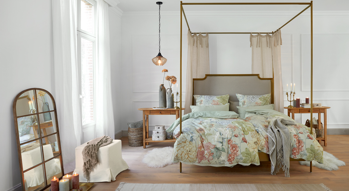 Himmelbett mit goldfarbener Metallrahmen und floraler Bettwäsche in hellem, gemütlichem Schlafzimmer