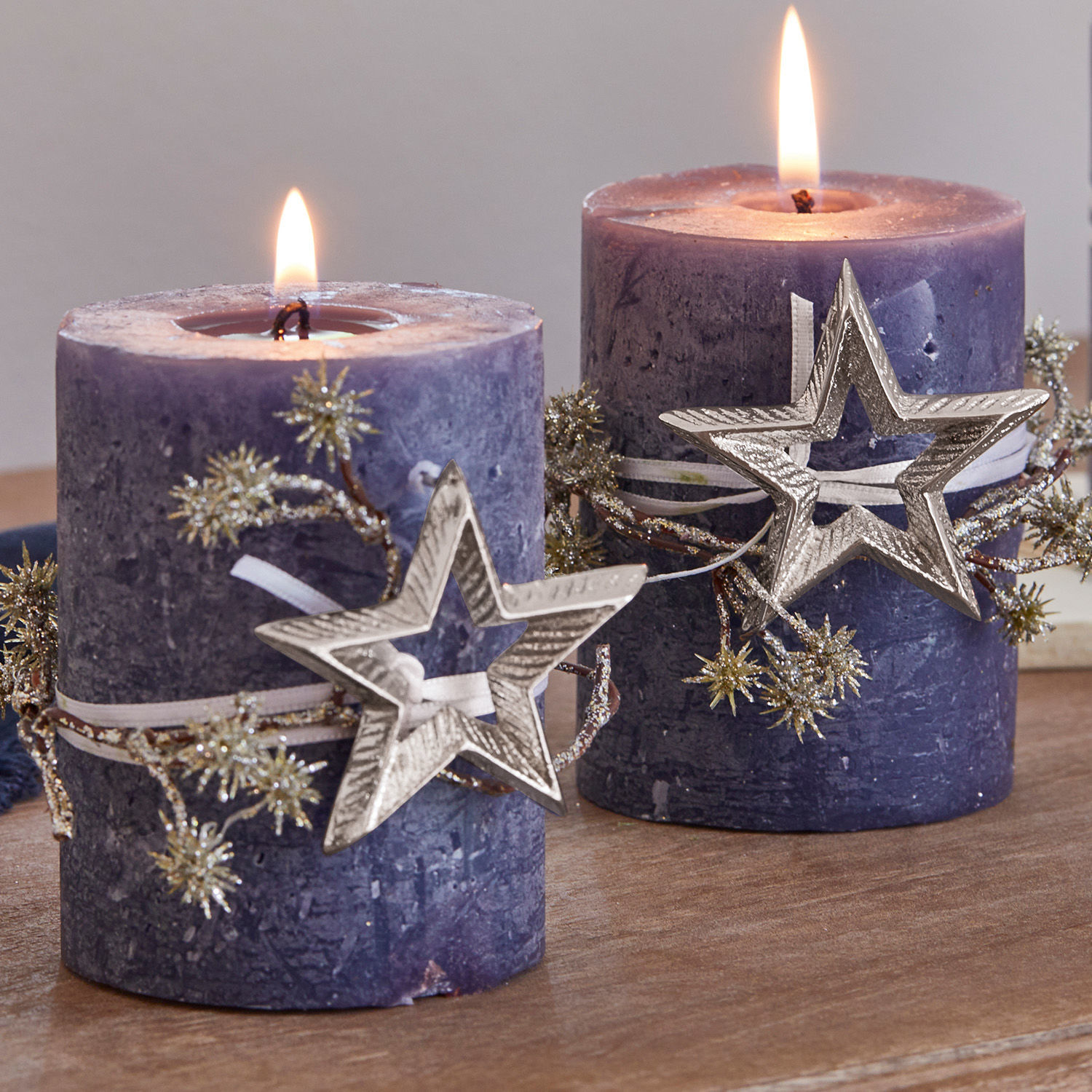 Zwei violette Kerzen mit Stern-Dekoration und glitzernden Zweigen auf Holztisch