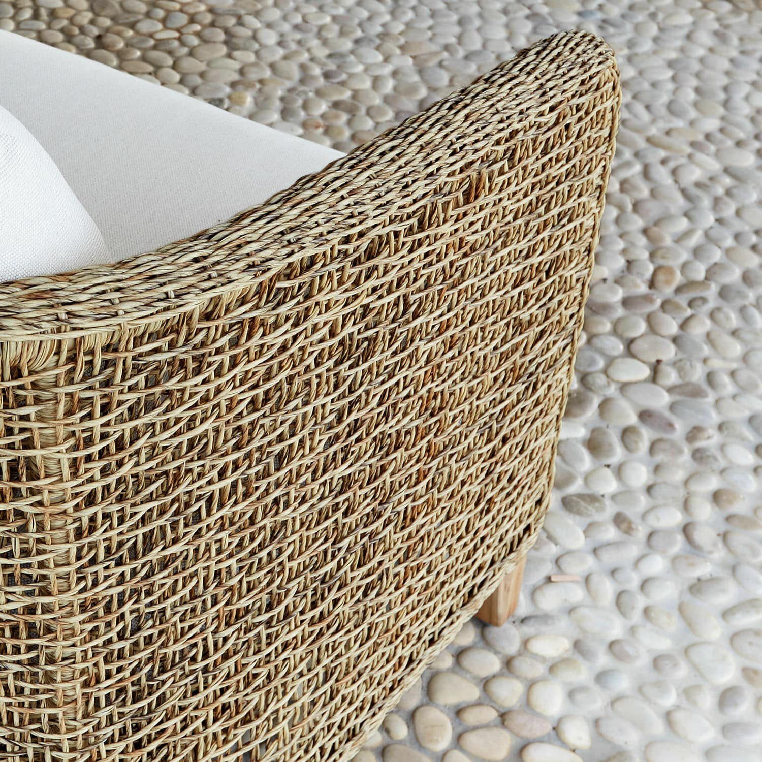 Natürlicher Korbsessel mit weißen Polstern auf Kiesboden, Outdoor-Möbel für Terrasse und Garten