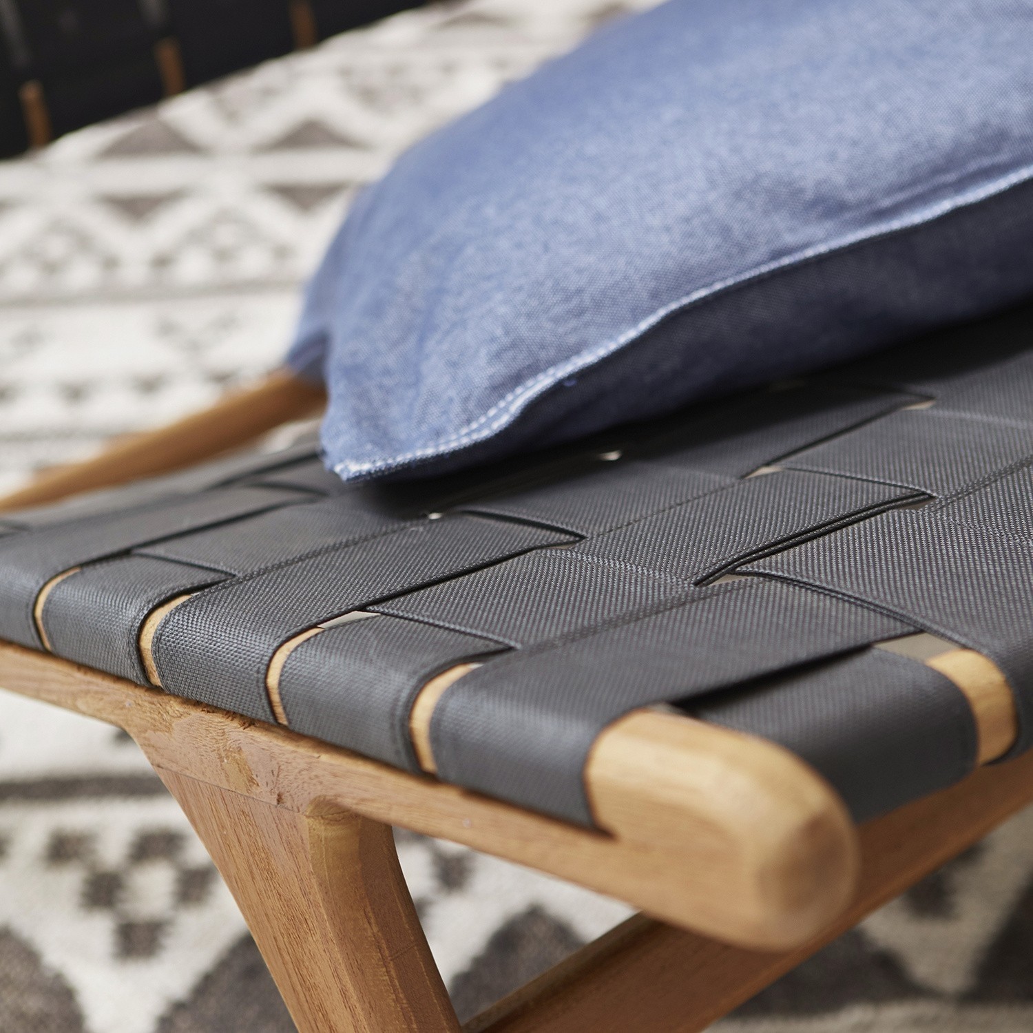 Hocker aus Holz mit schwarzem geflochtenem Sitz und blauem Kissen auf gemustertem Teppich