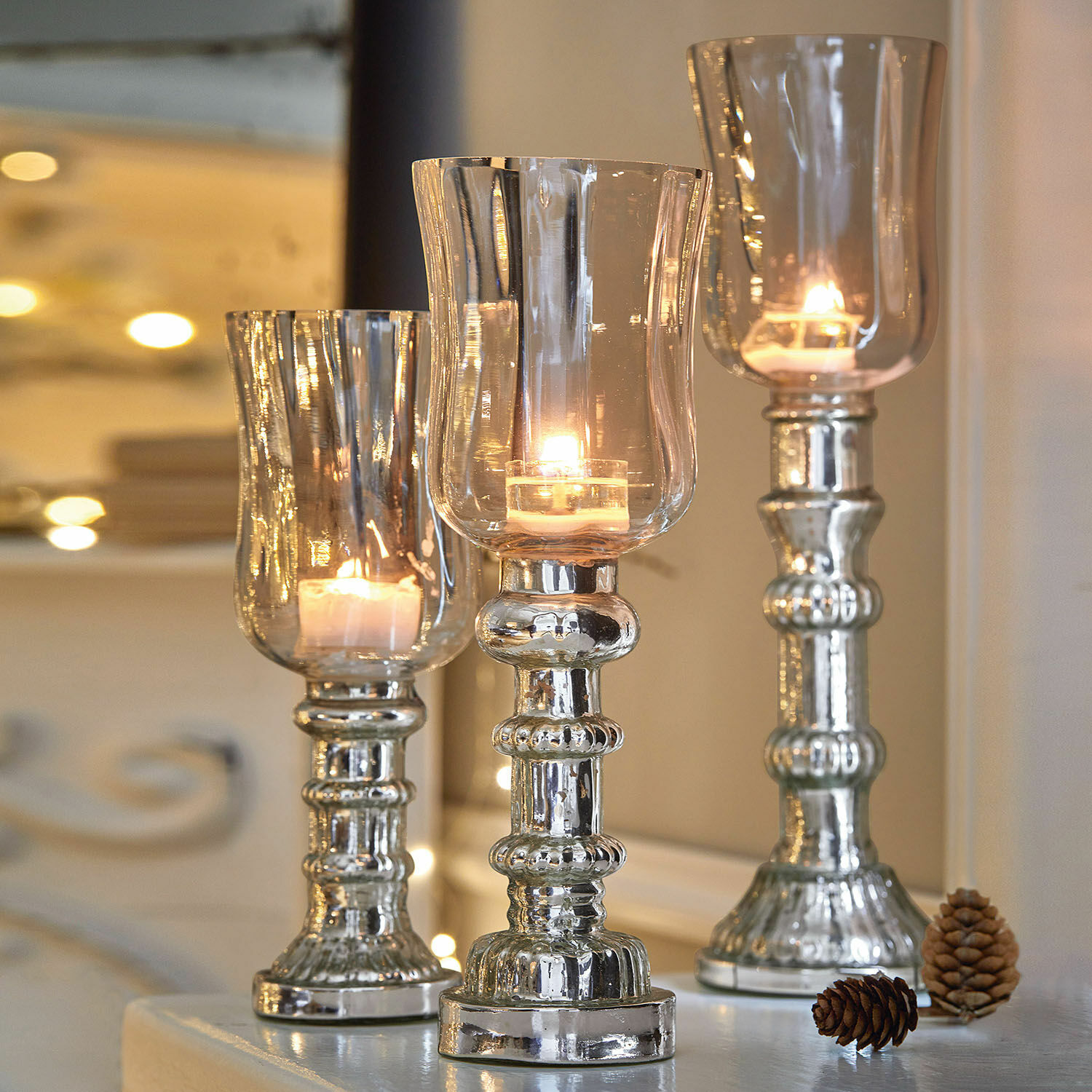 Windlicht 3er Set Fréjeville Drei silberne Kerzenhalter aus Glas und Metall mit brennenden Kerzen und dekorativen Kiefernzapfen