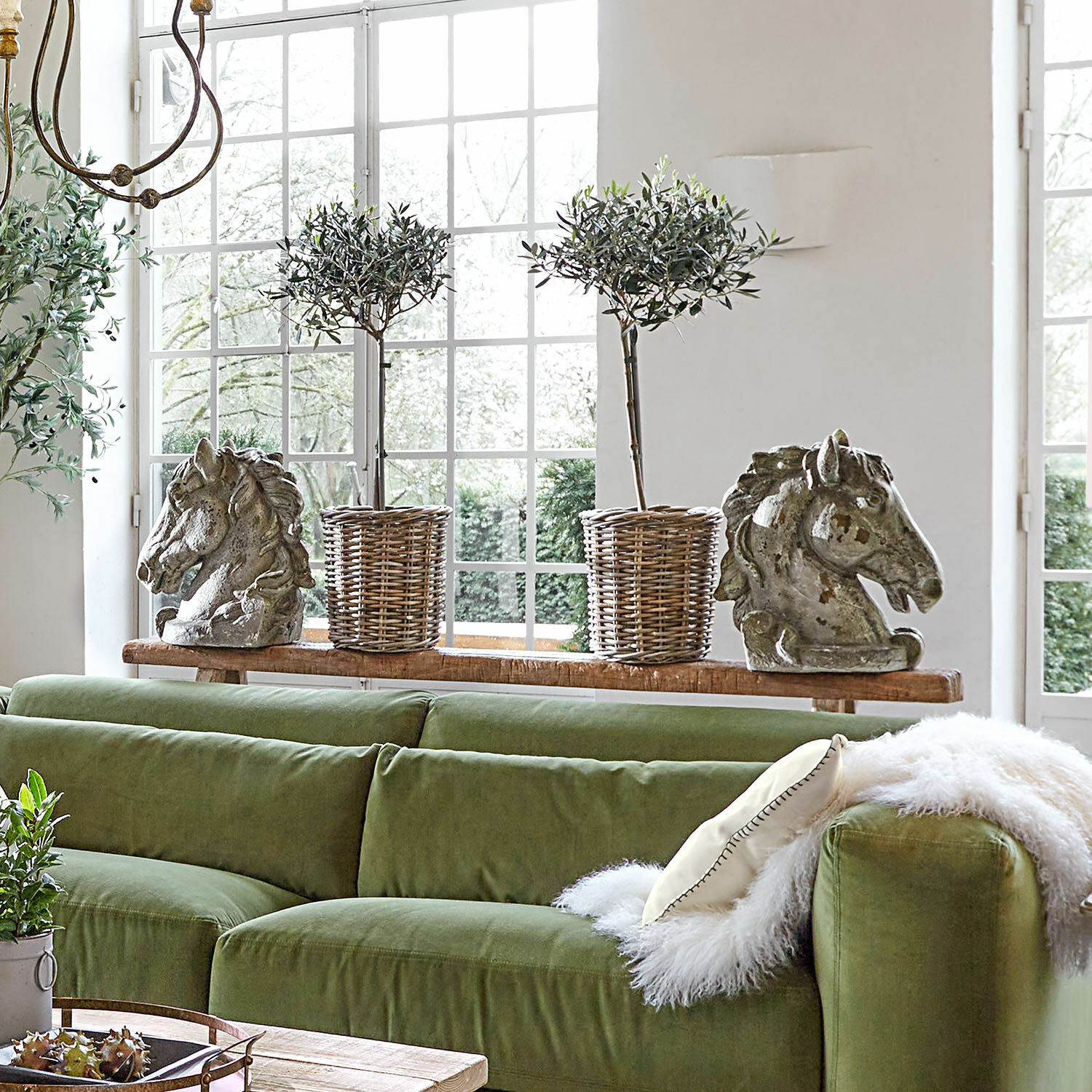 Grünes Samtsofa mit dekorativen Kissen und Pferdekopf-Skulpturen auf Holzregal im Wohnzimmer