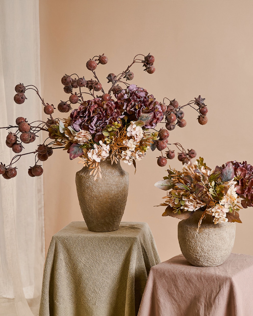 Zwei steinerne Vasen mit herbstlichen Blumen und getrockneten Früchten in warmen Beige- und Brauntönen als Dekoration