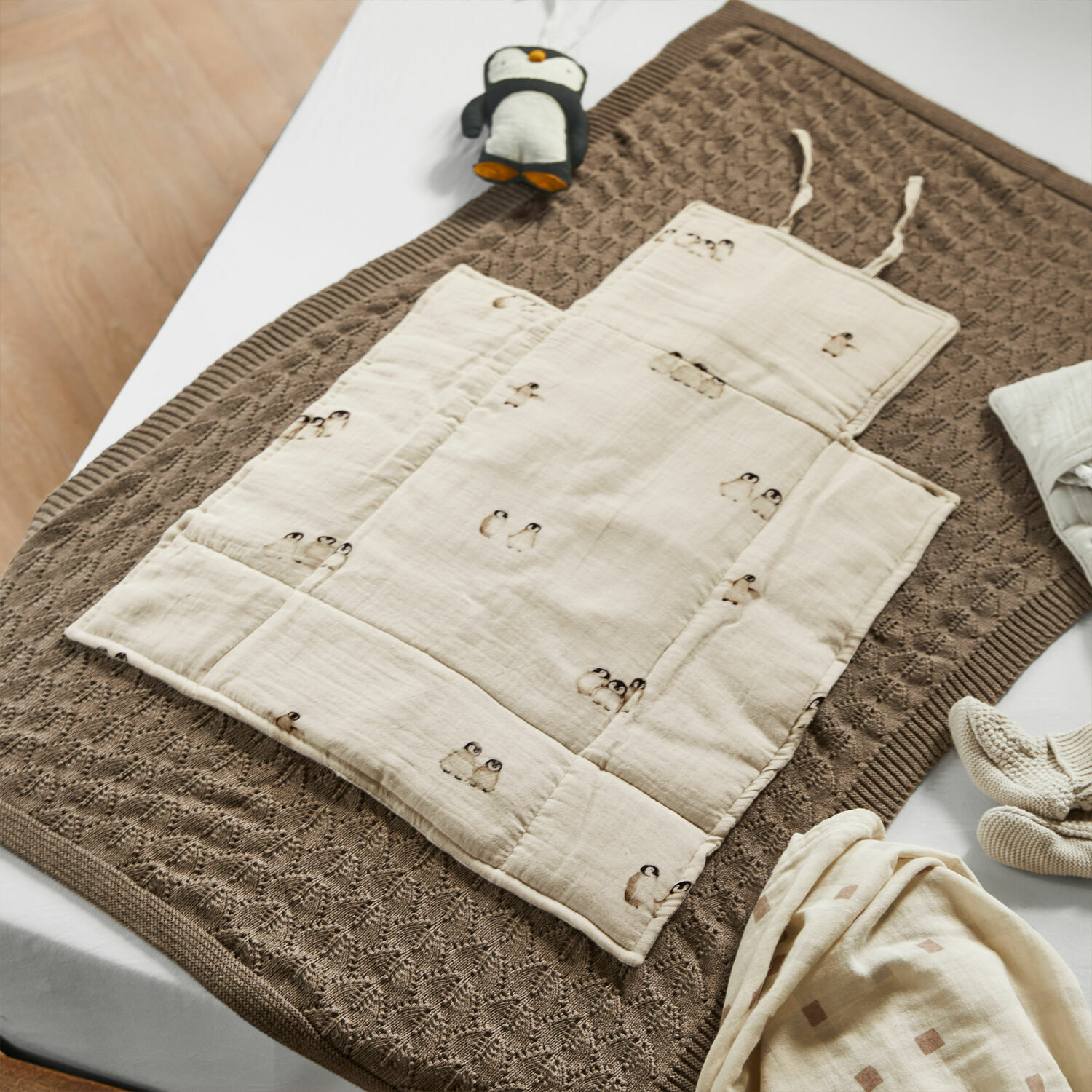 Beige Baumwoll-Kinderkrabbelmatte mit Pinguin-Motiv auf braunem Strickdecke, Babyzubehör