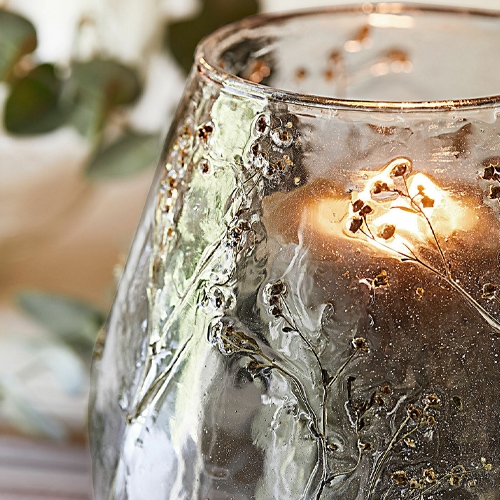 Glaswindlicht mit floraler Reliefdekoration und warmem Kerzenlicht als Wohnaccessoire
