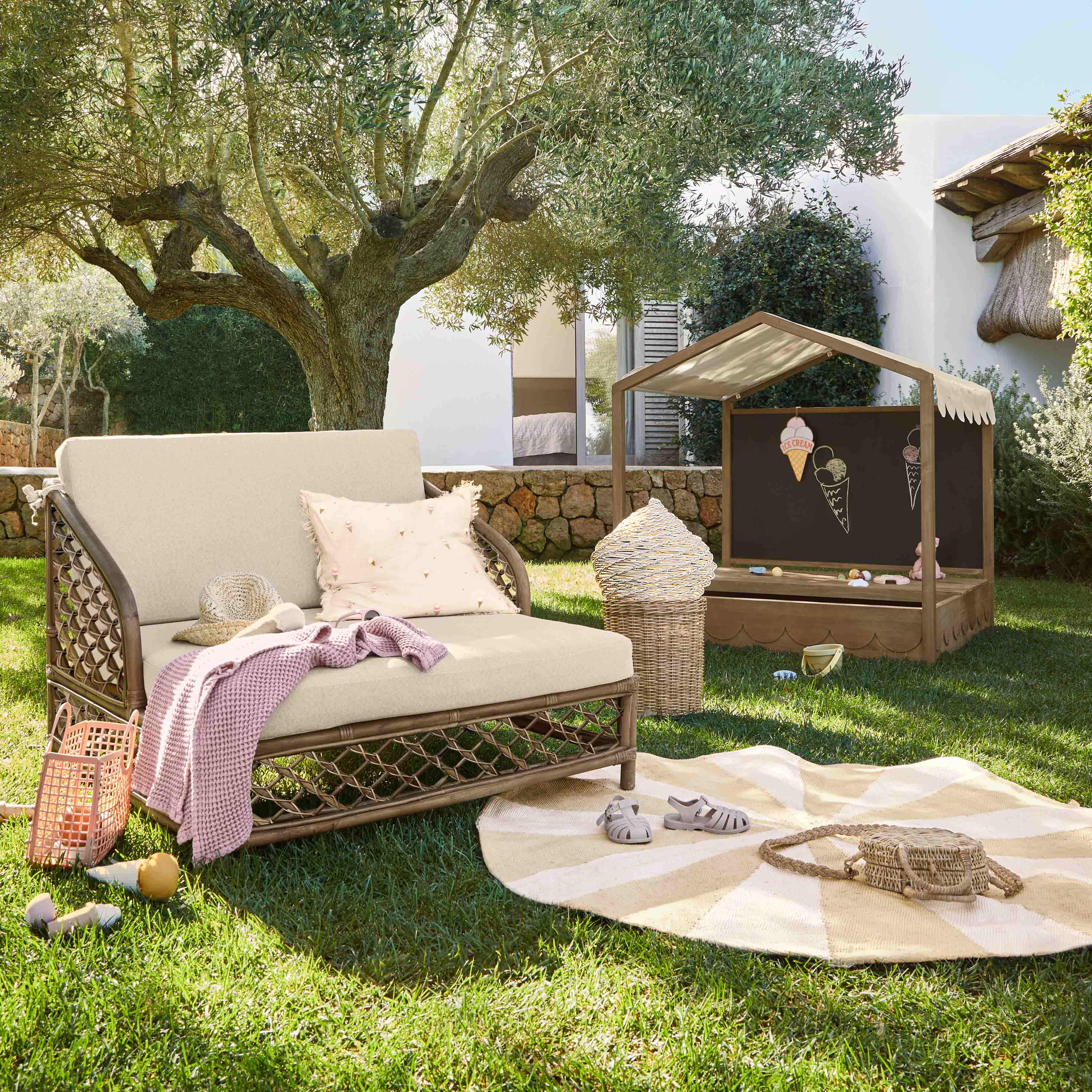 Gartenmöbel aus Rattan mit beigen Polstern und Kinderspielhaus auf Rasen in sonnigem Garten