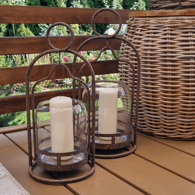 Zwei dekorative Laternen mit Metallrahmen und weißen Kerzen auf einem Holztisch im Garten