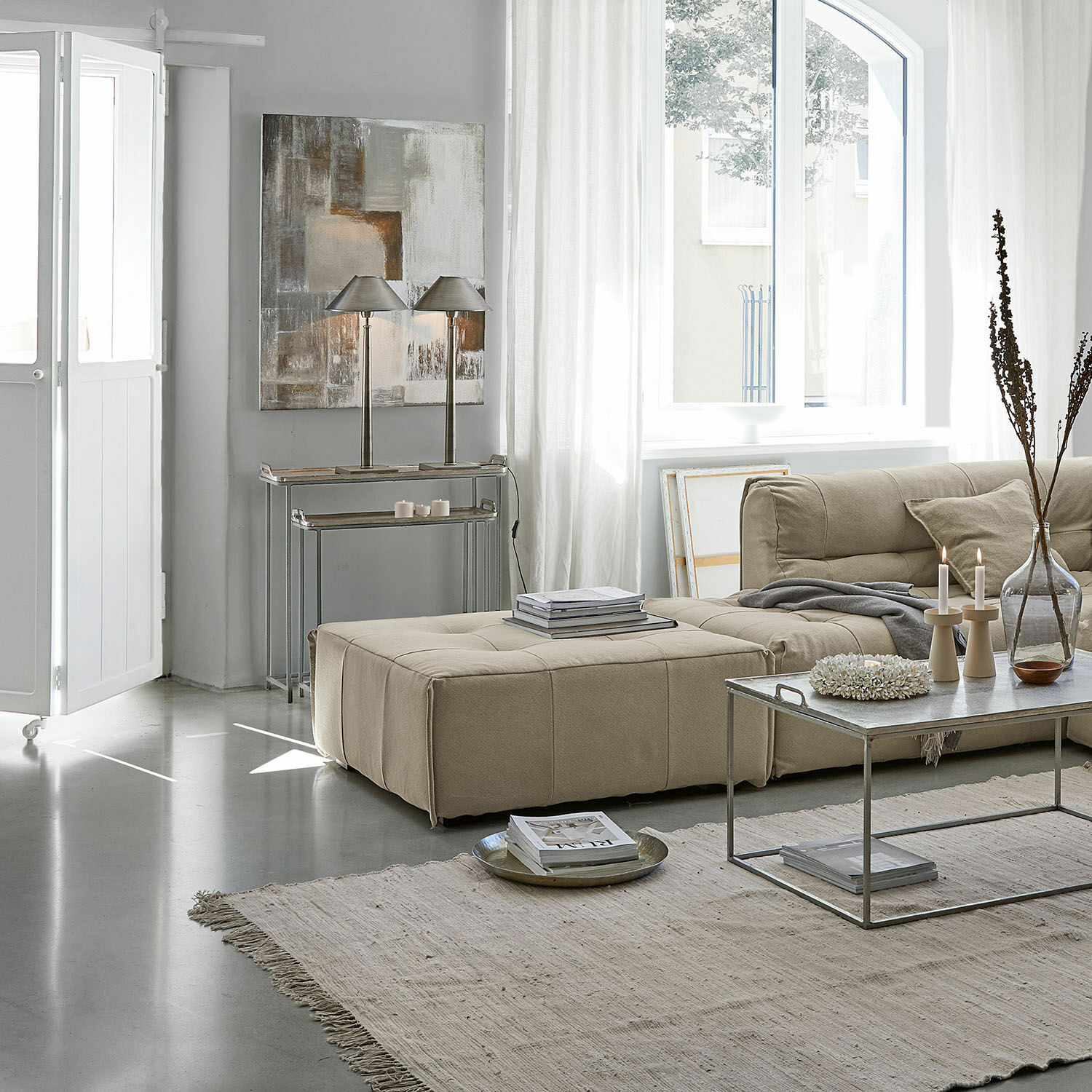 Beige gepolsterte Couch und Hocker im hellen Wohnzimmer mit Metall-Couchtisch und Dekorationen