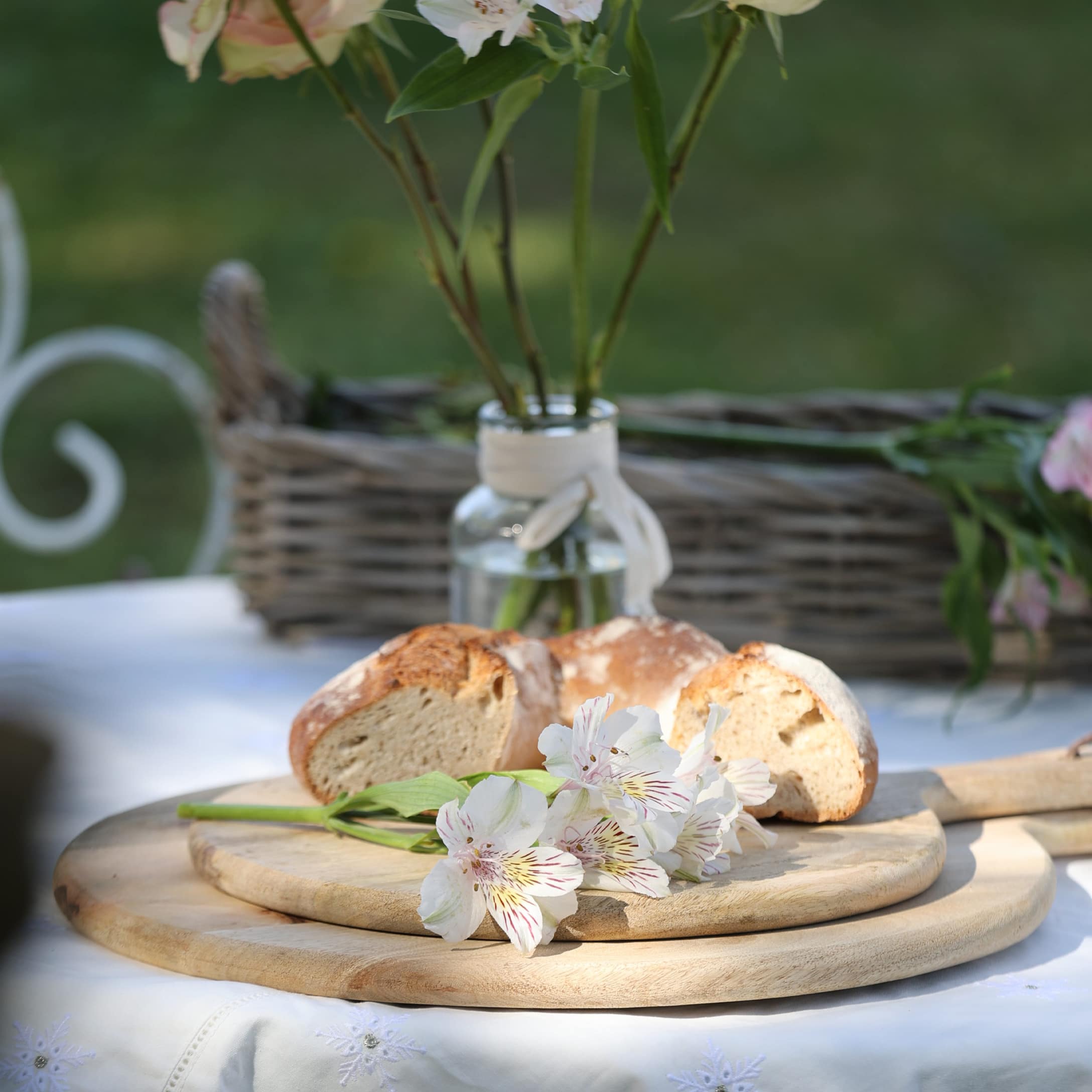 Holzschneidebrett mit weißen Blumen und Brot auf weiß gedecktem Tisch im Garten