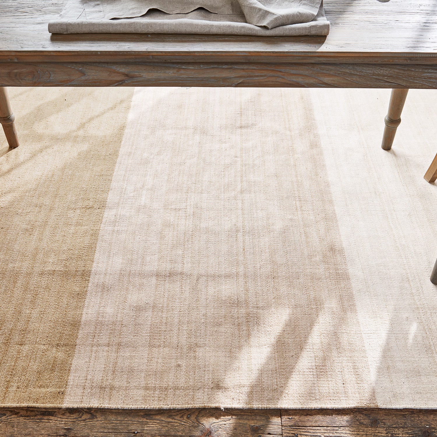 Naturmaterial-Teppich in beigen Farbtönen unter einem Holztisch auf Holzboden