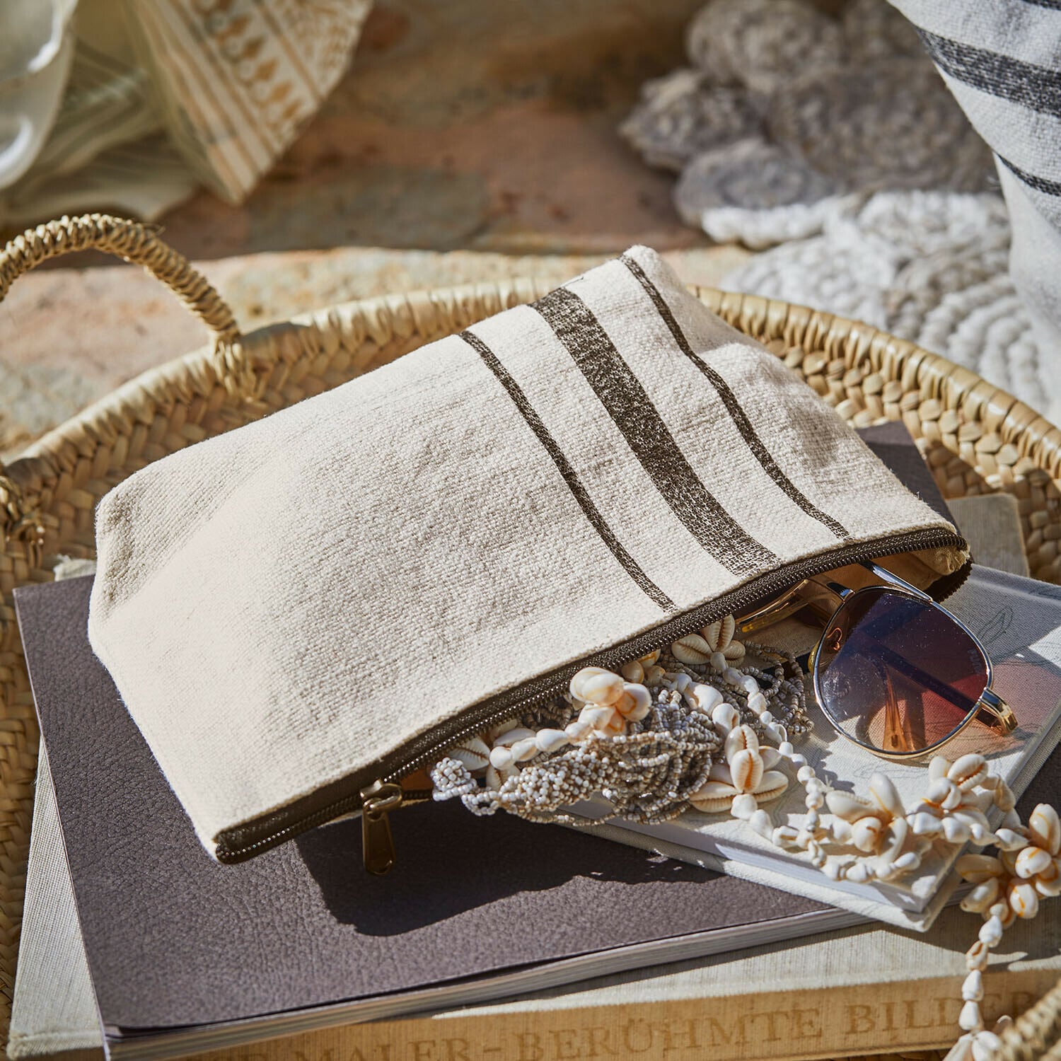 Beige Baumwoll-Kosmetiktasche mit braunen Streifen auf Korb mit Sonnenbrille und Schmuck