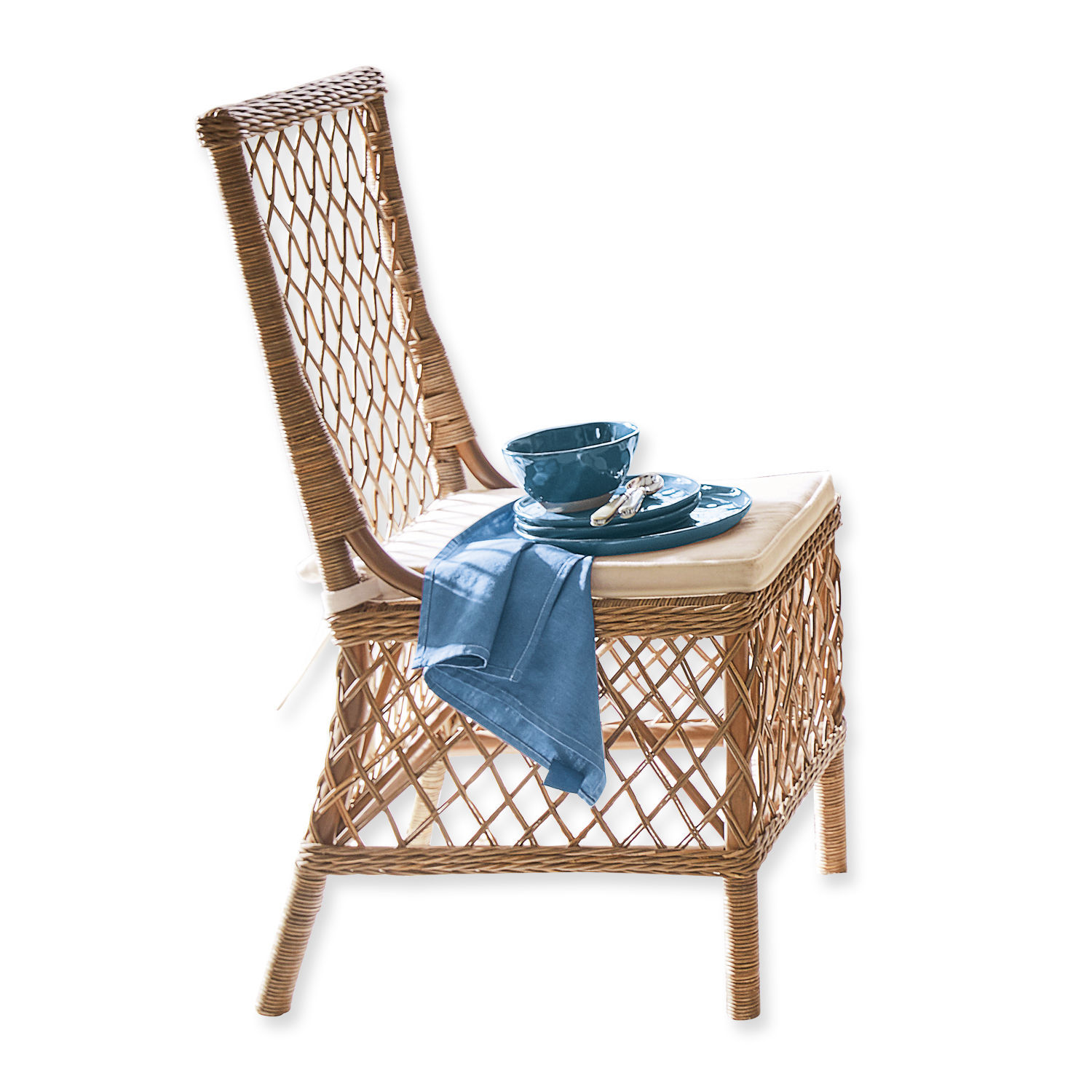 Rattanstuhl in Naturfarbe mit beigem Sitzkissen und blauer Geschirrdeko auf dem Sitz