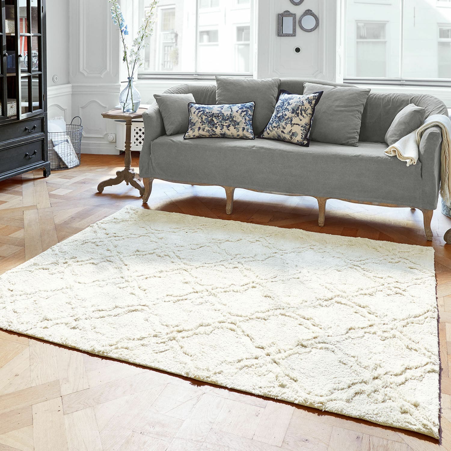 Teppich Petrus Heller cremefarbener Teppich mit weichem Muster im Wohnzimmer mit grauem Sofa und Holzfußboden