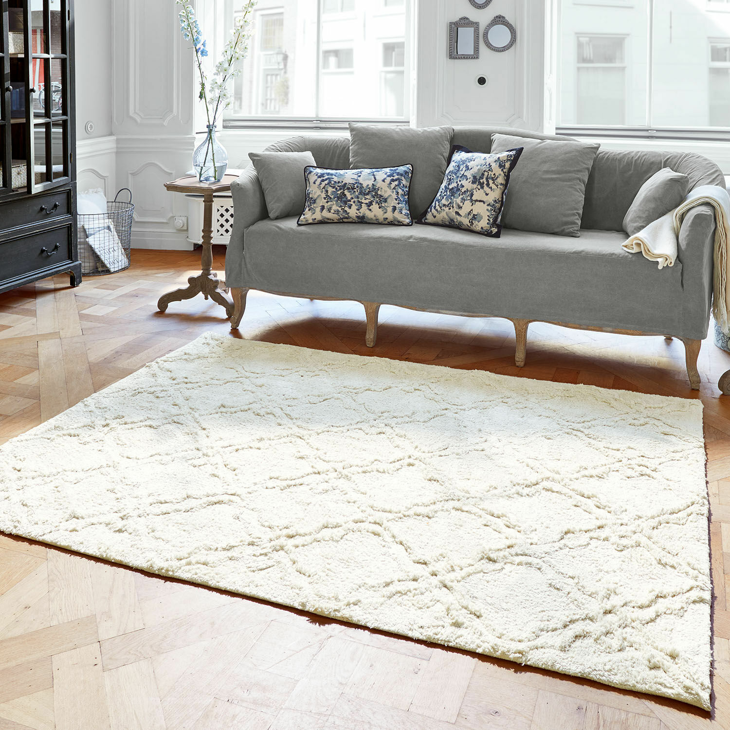Teppich Petrus Heller cremefarbener Teppich mit weichem Muster im Wohnzimmer mit grauem Sofa und Holzfußboden