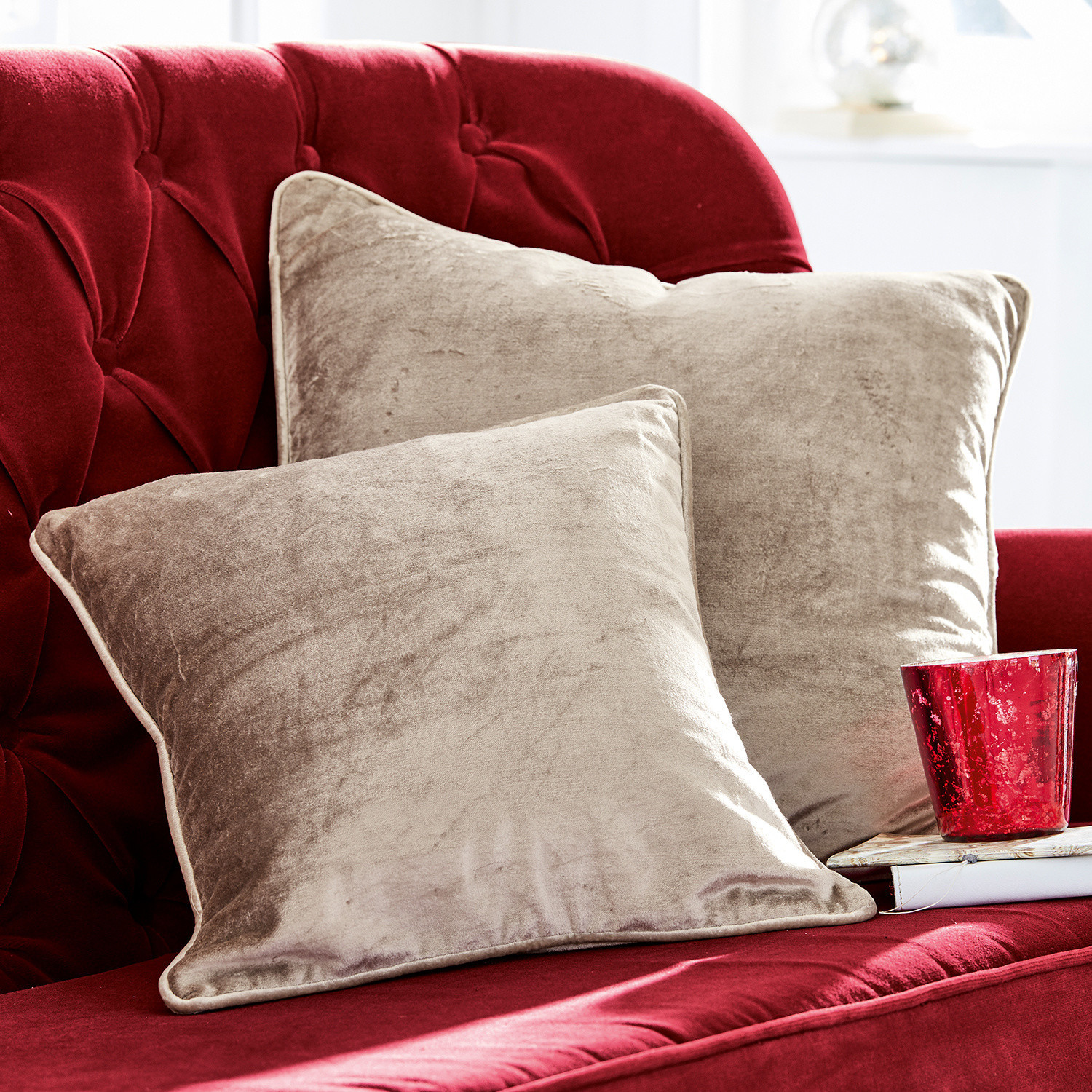 Beige Samtkissen auf rotem Samtsofa, weiche Wohnraumdekoration aus samtigem Material