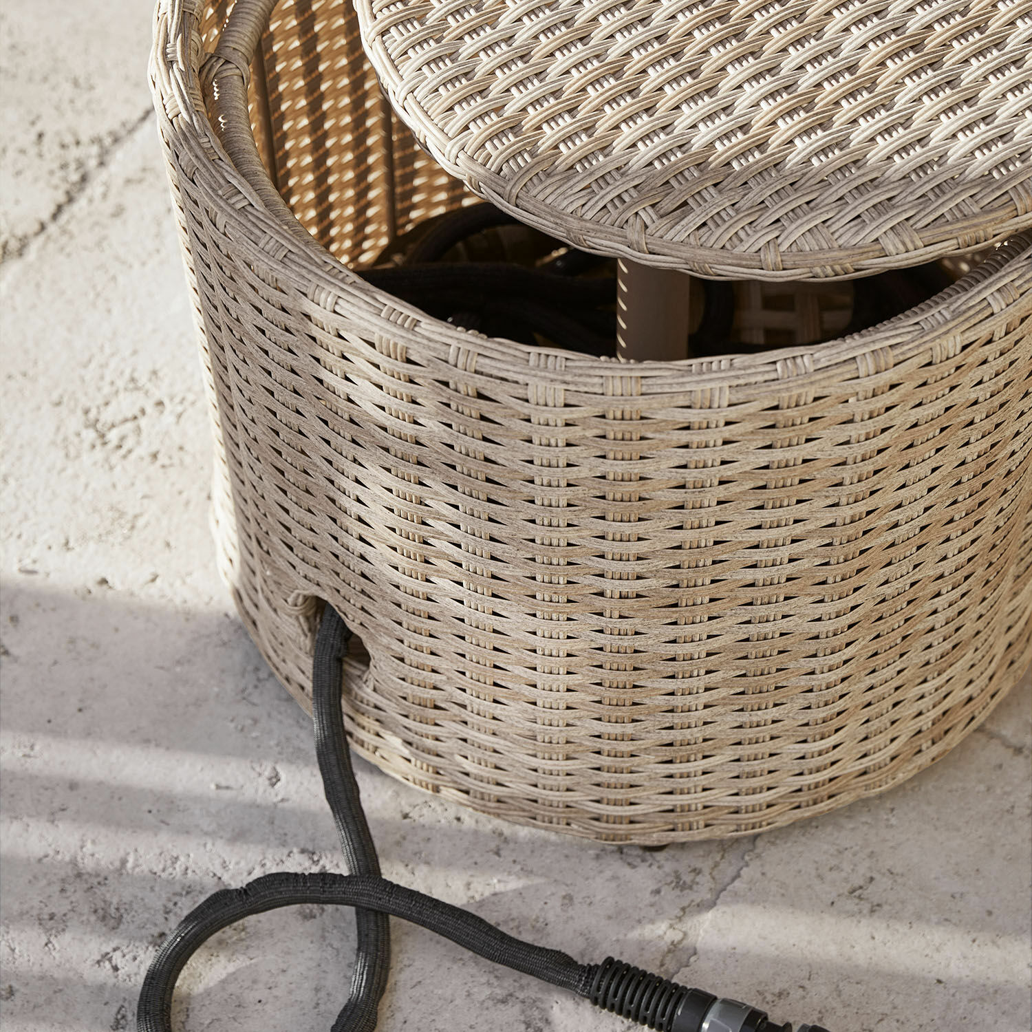 Runder Beistelltisch aus hellem Rattan mit sichtbarem Stromkabel auf Betonboden