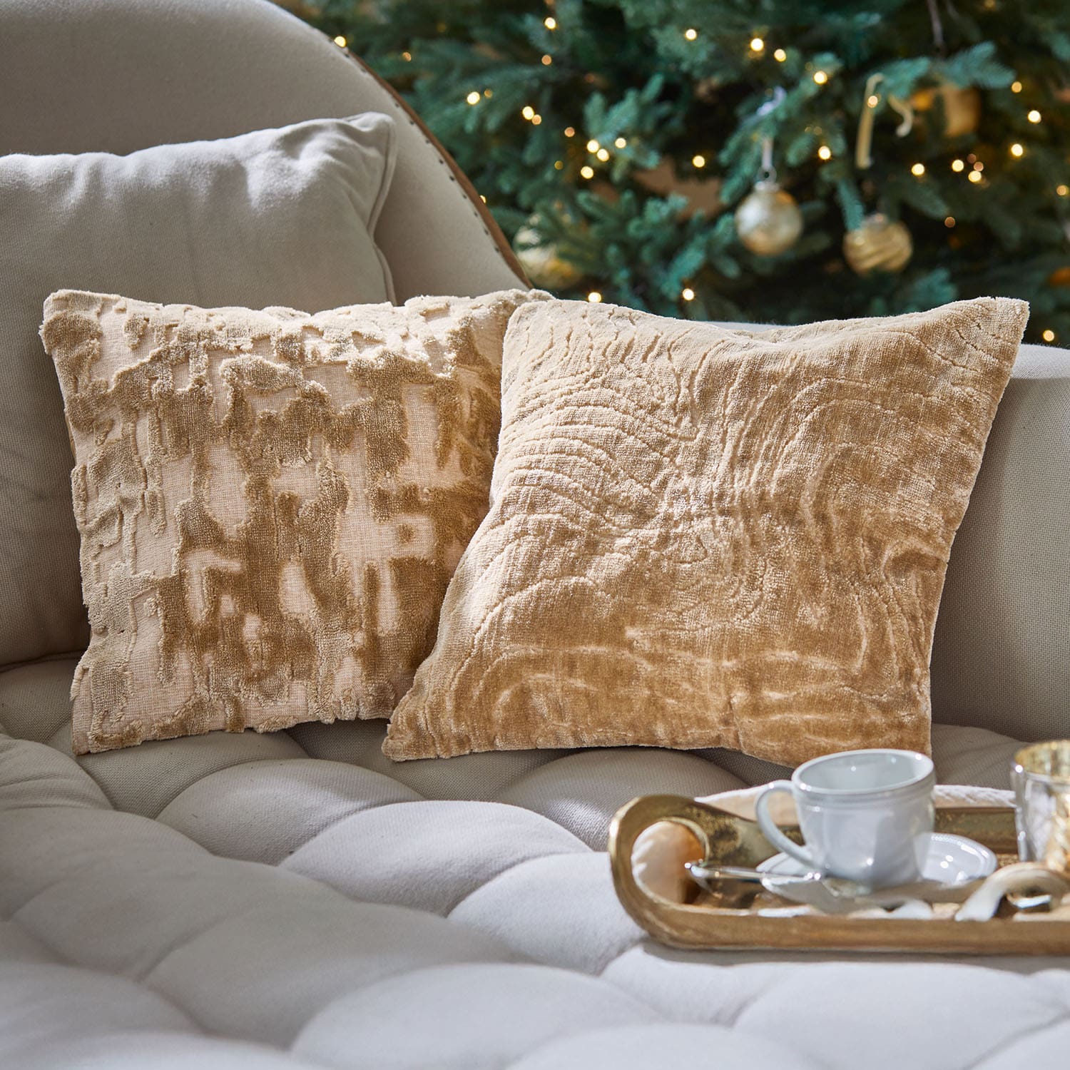 Zwei beige dekorative Kissen aus weichem Material auf hellem Sofa vor festlich geschmücktem Christbaum