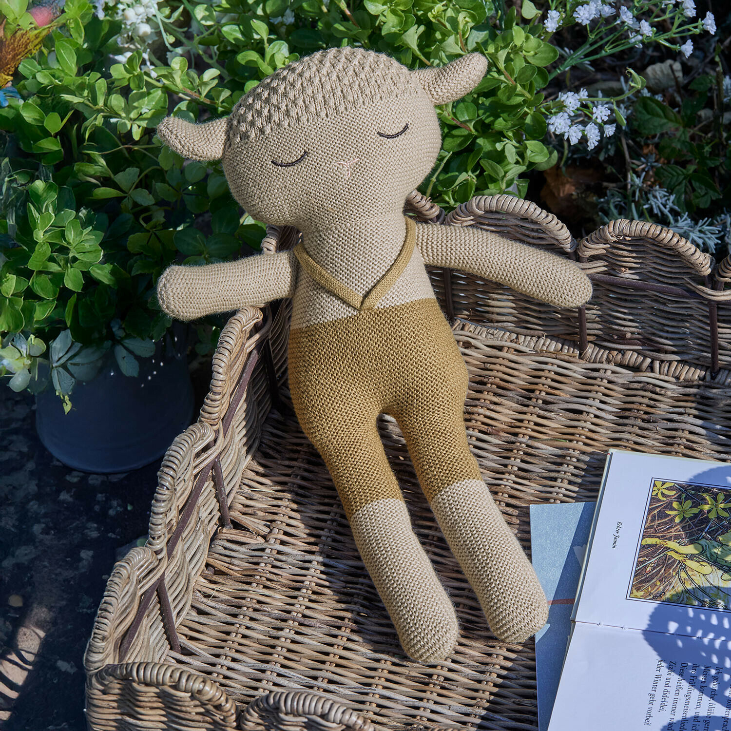 Stofftier Cuddlecloud Beige gestricktes Schaf Kuscheltier im Weidenkorb neben Buch im Garten