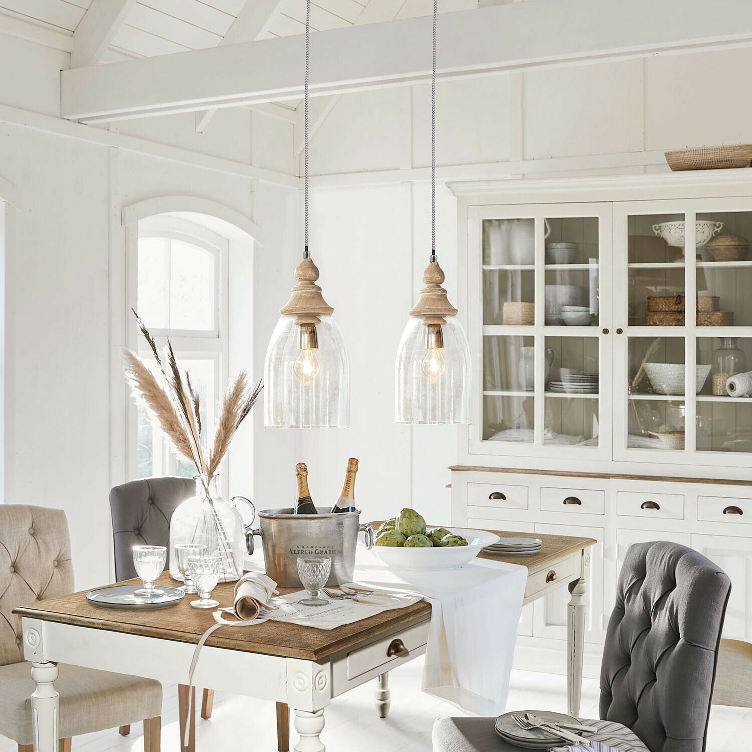 Rustikaler Essbereich mit weißem Holztisch, grauen Polsterstühlen und Vitrinenschrank mit Korbdeko