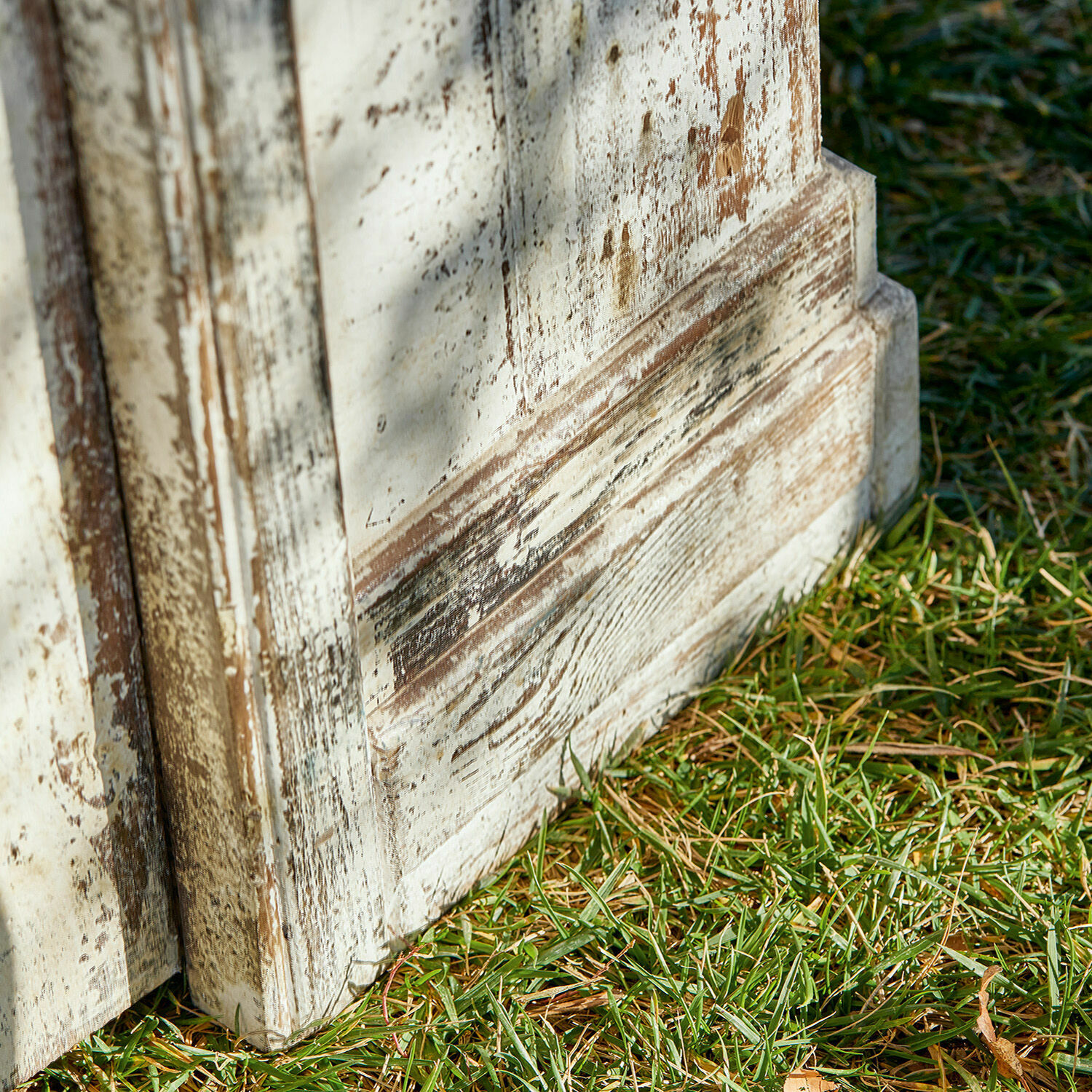 Nahaufnahme eines weiß lackierten, antik wirkenden Holzmöbels mit sichtbarer Maserung auf Gras