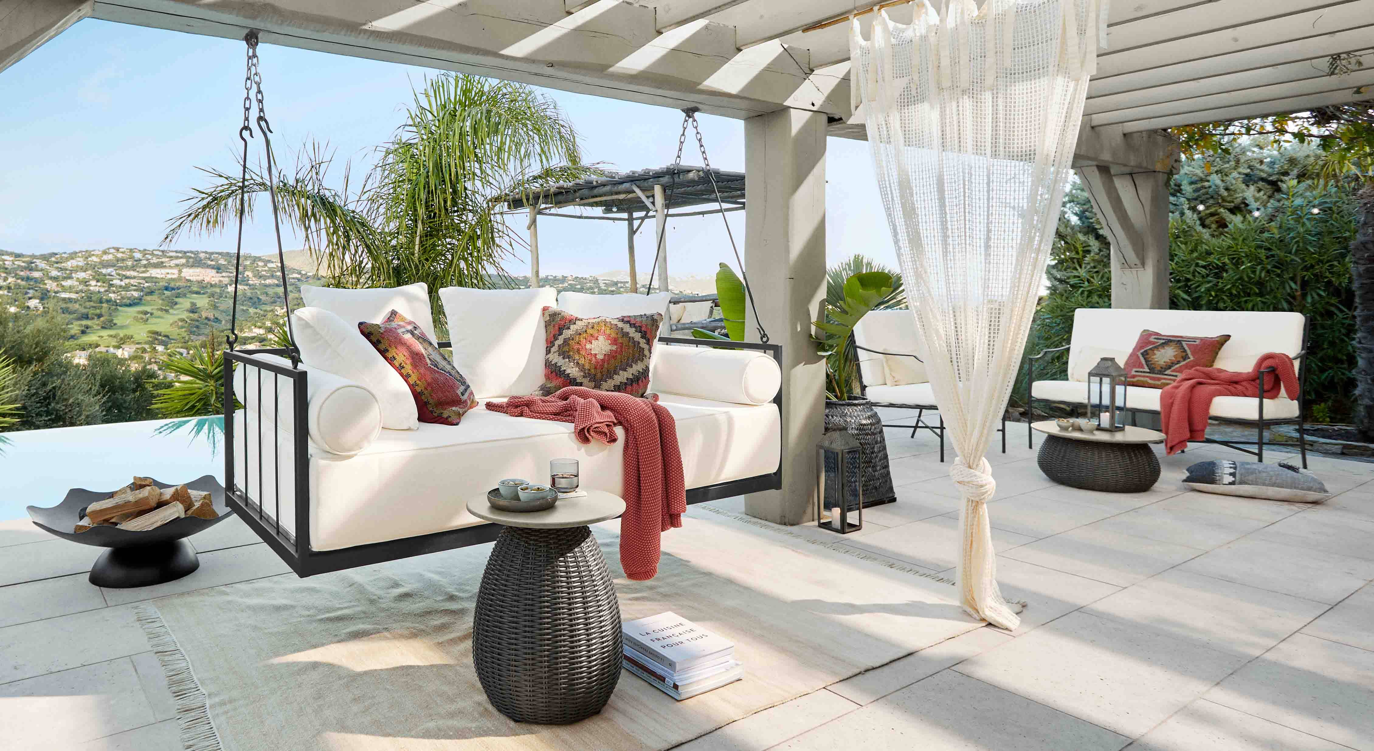 Weiße Hängesofa mit Metallrahmen und bunten Kissen auf Terrasse mit Hügelblick