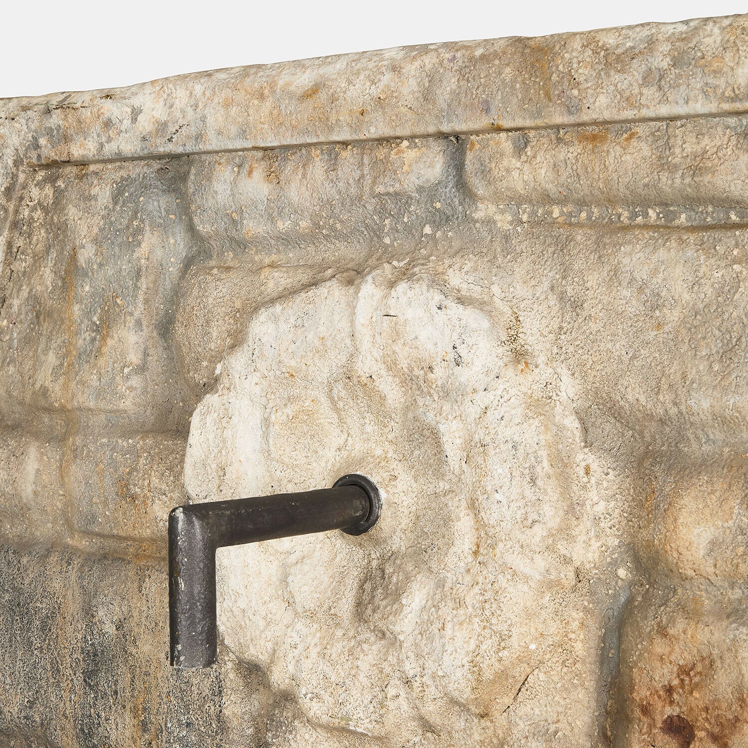 Steinmauer mit reliefartigem Motiv und schwarzem Metallwasserhahn im rustikalen Gartenstil