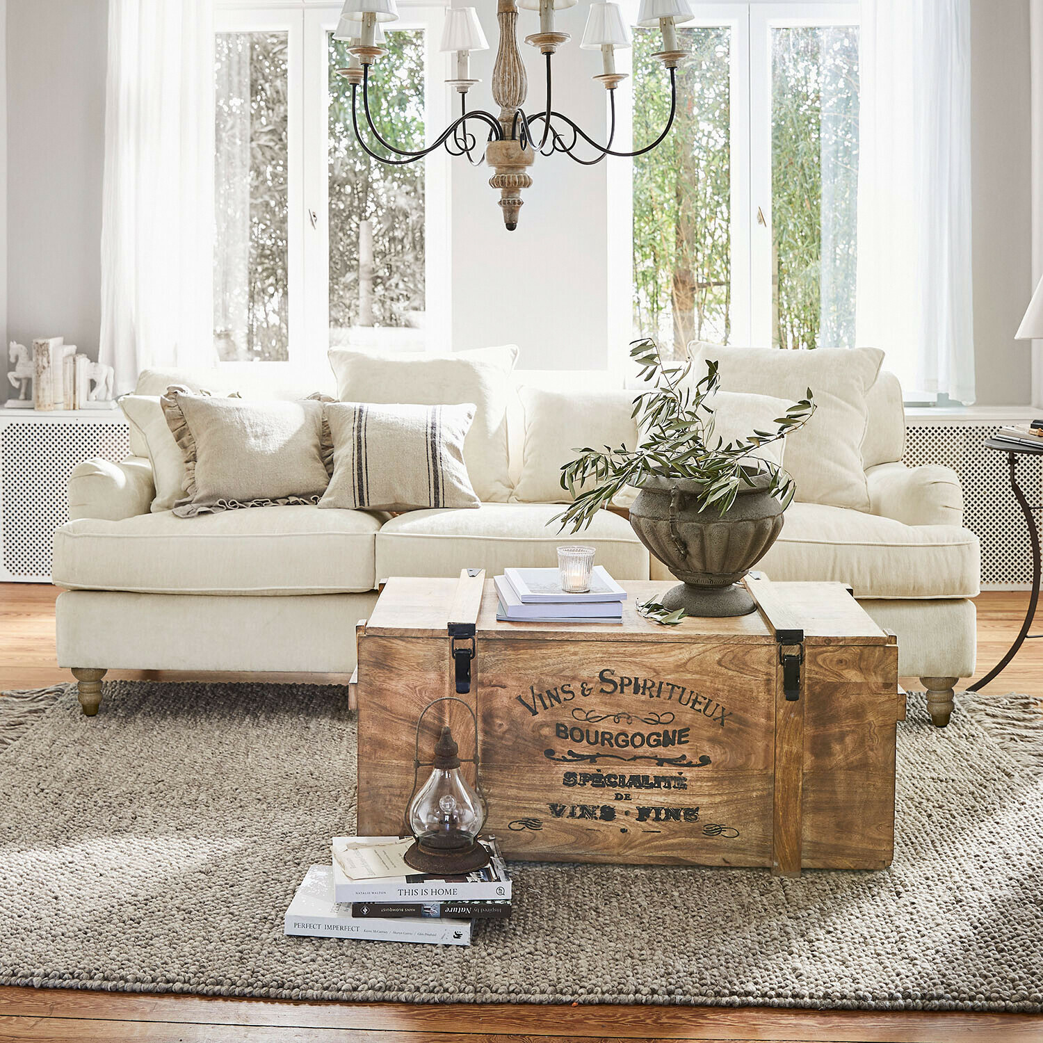 Sofa Isa Holztruhe mit Vintage-Schriftzug als Couchtisch im hellen Wohnzimmer mit beigem Sofa und Dekoration