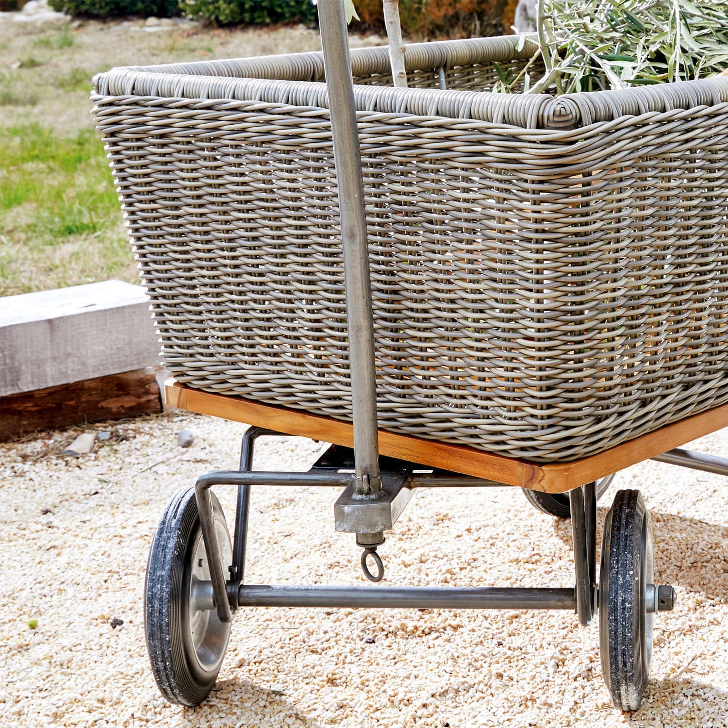 Gartenwagen aus grauem Rattan mit Metallrädern und Holzrahmen auf Kiesboden