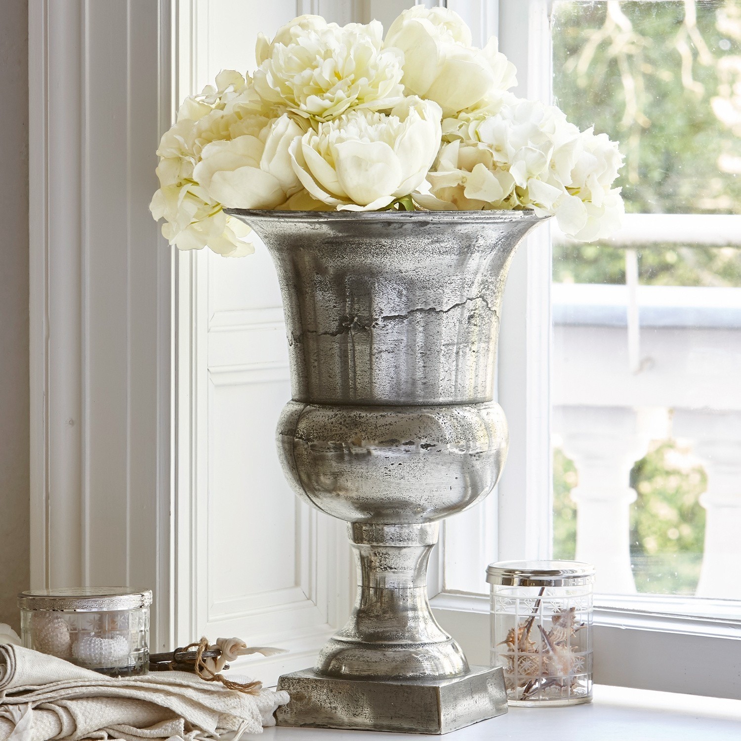 Dekorativer silberner Metallvase mit weißen Blumen auf Fensterbank, stilvolles Wohnaccessoire