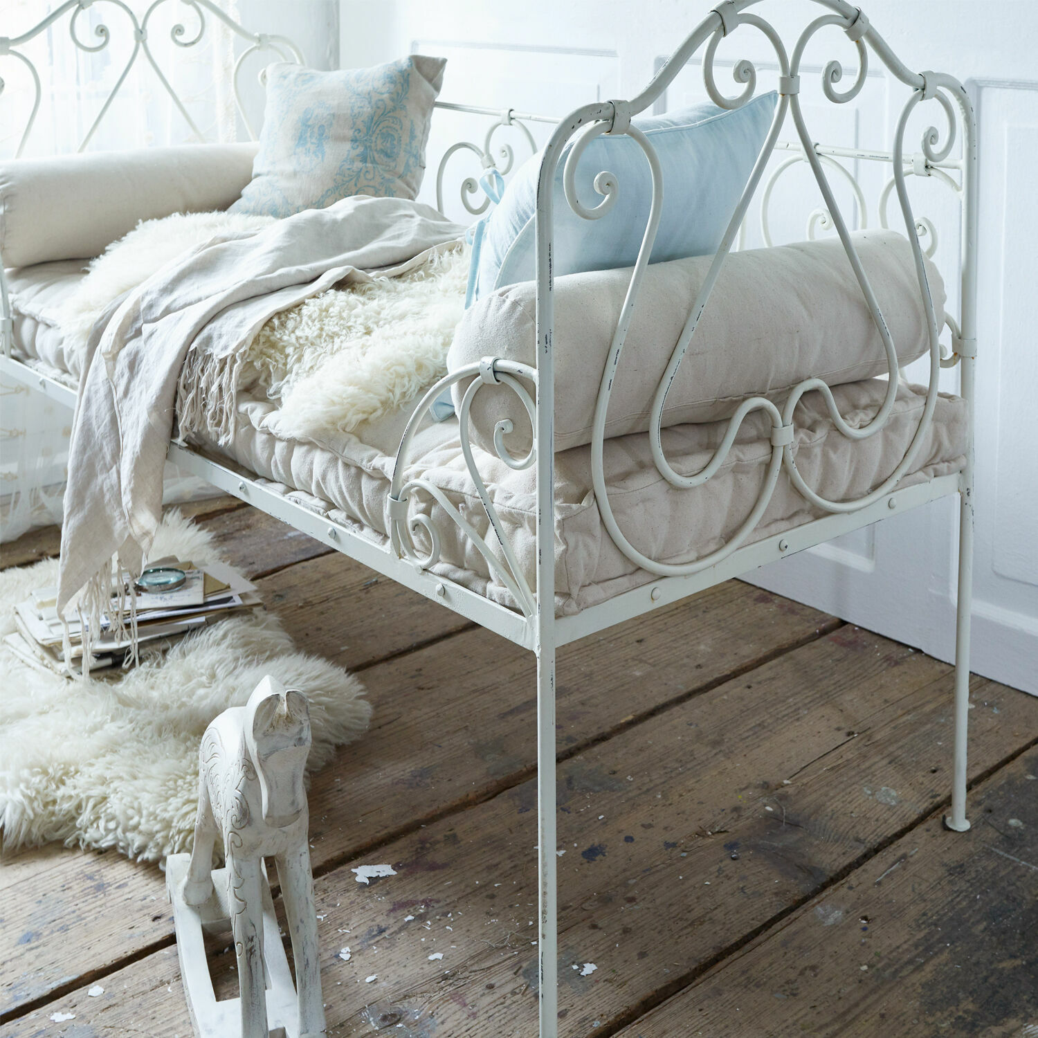 Weiße Metallsofa mit weichen Kissen und Decke auf Vintage-Holzboden im Wohnraum