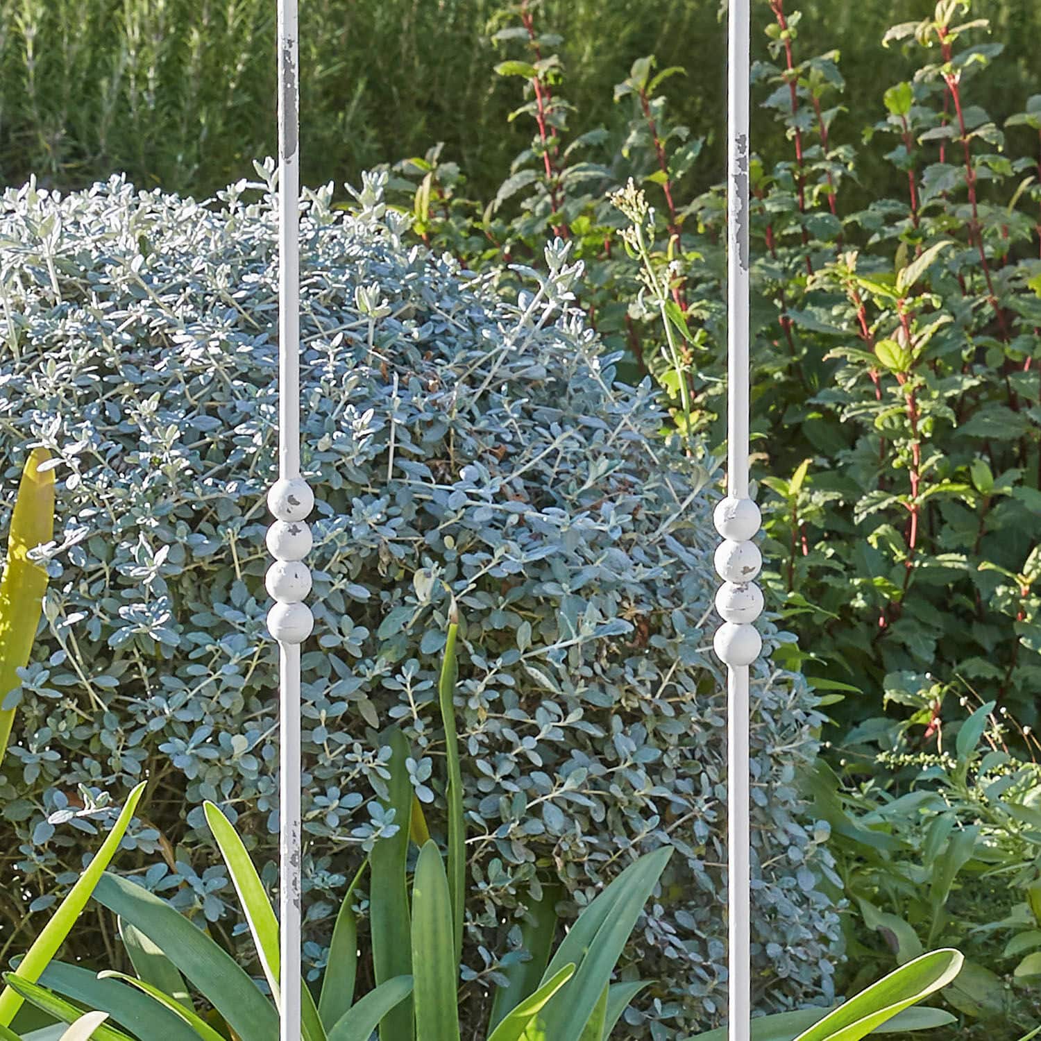 Weißer Metallstab mit kugelförmigen Verzierungen vor grünem Pflanzen- und Strauchhintergrund