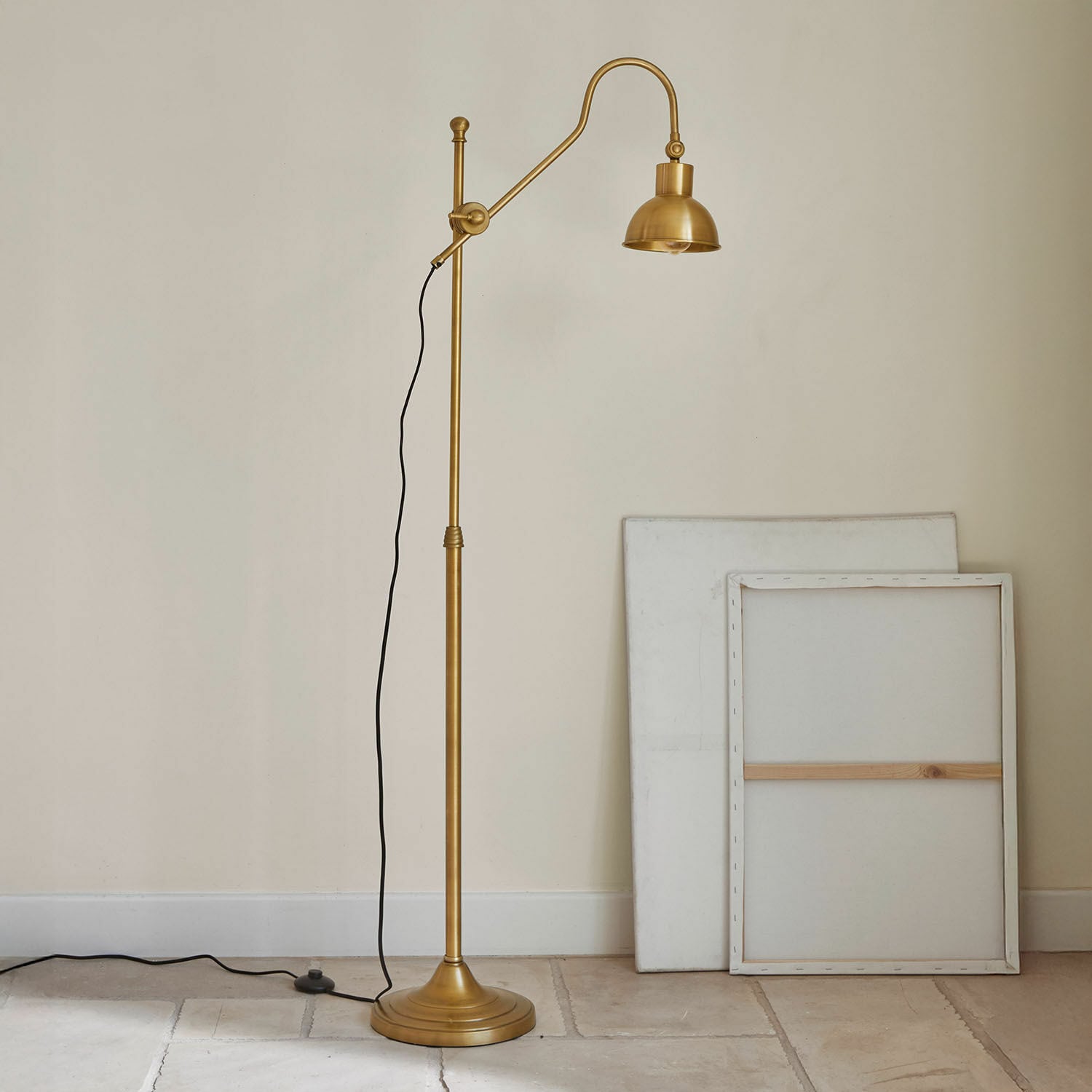 Goldfarbene Stehlampe aus Metall mit verstellbarem Arm und schwarzem Kabel vor hellem Hintergrund