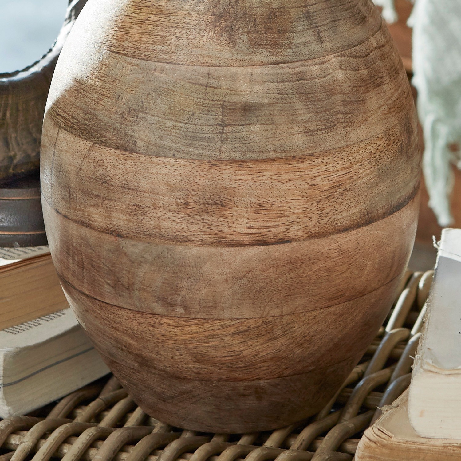 Dekorativer Mango-Holzvase in Naturfarbe auf Rattantisch mit Büchern arrangiert