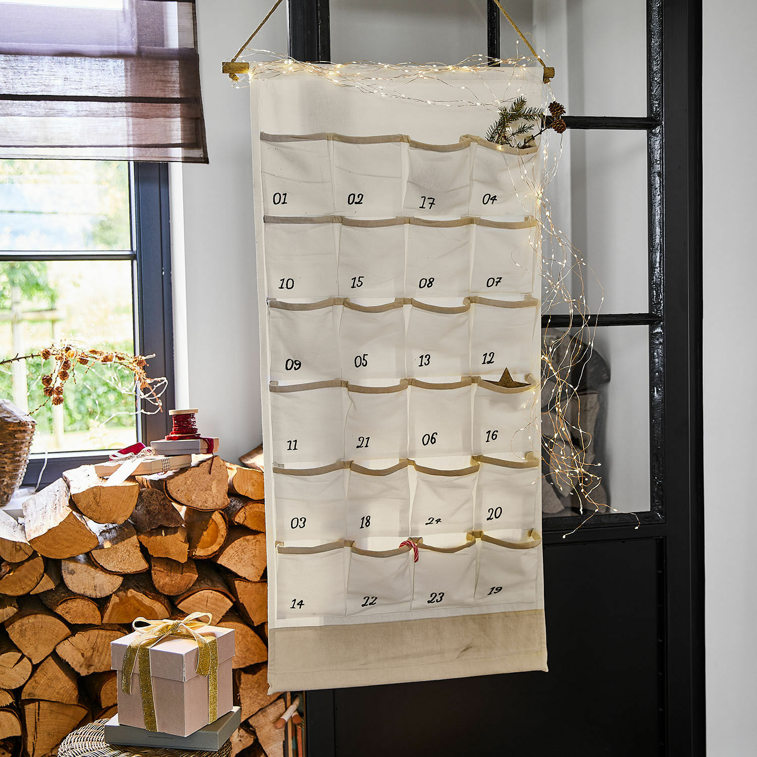 Beiger Adventskalender aus Stoff mit 24 nummerierten Taschen und Weihnachtsdeko im Raum