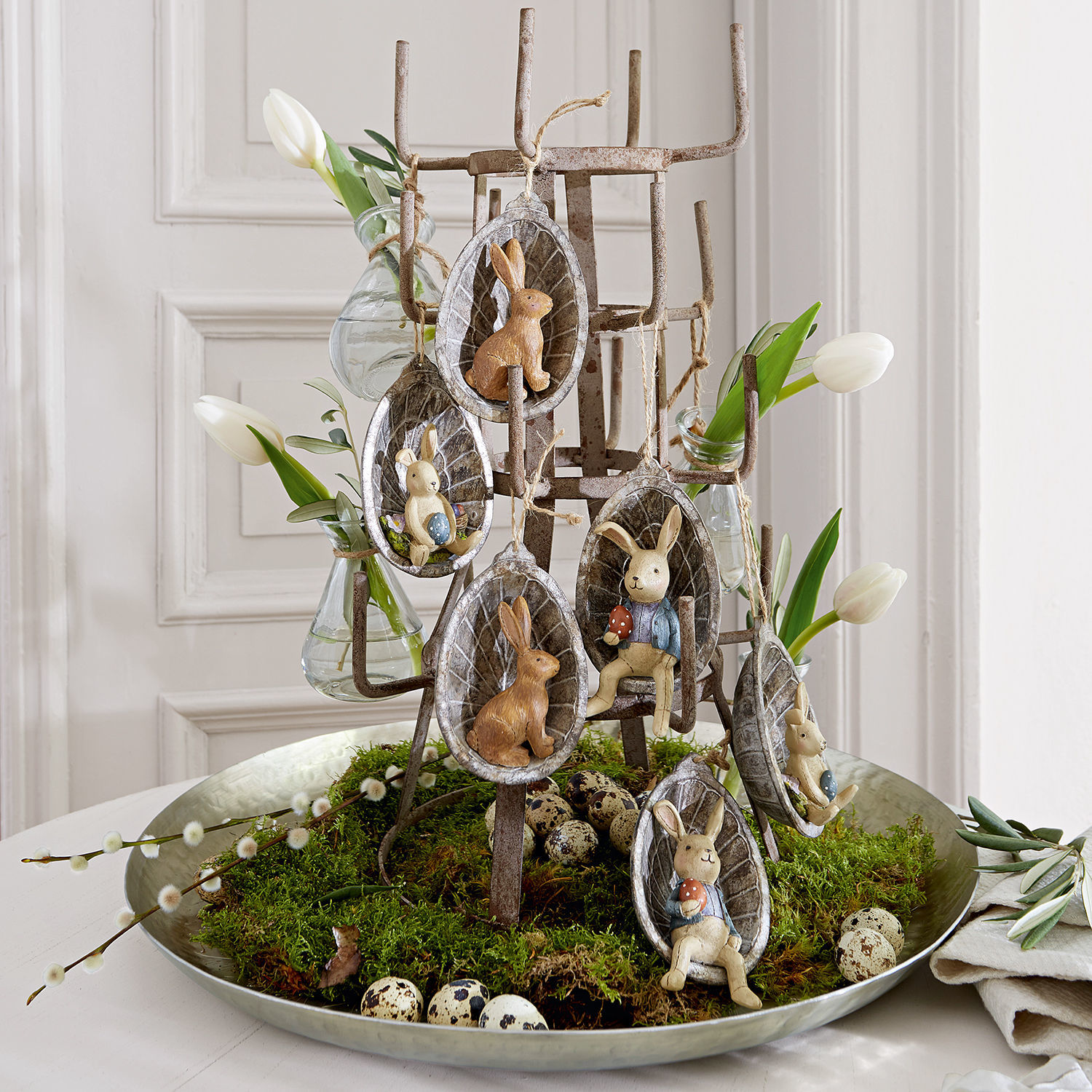 Osterdekoration mit Keramikhasen und weißen Tulpen auf Metallständer mit Moos