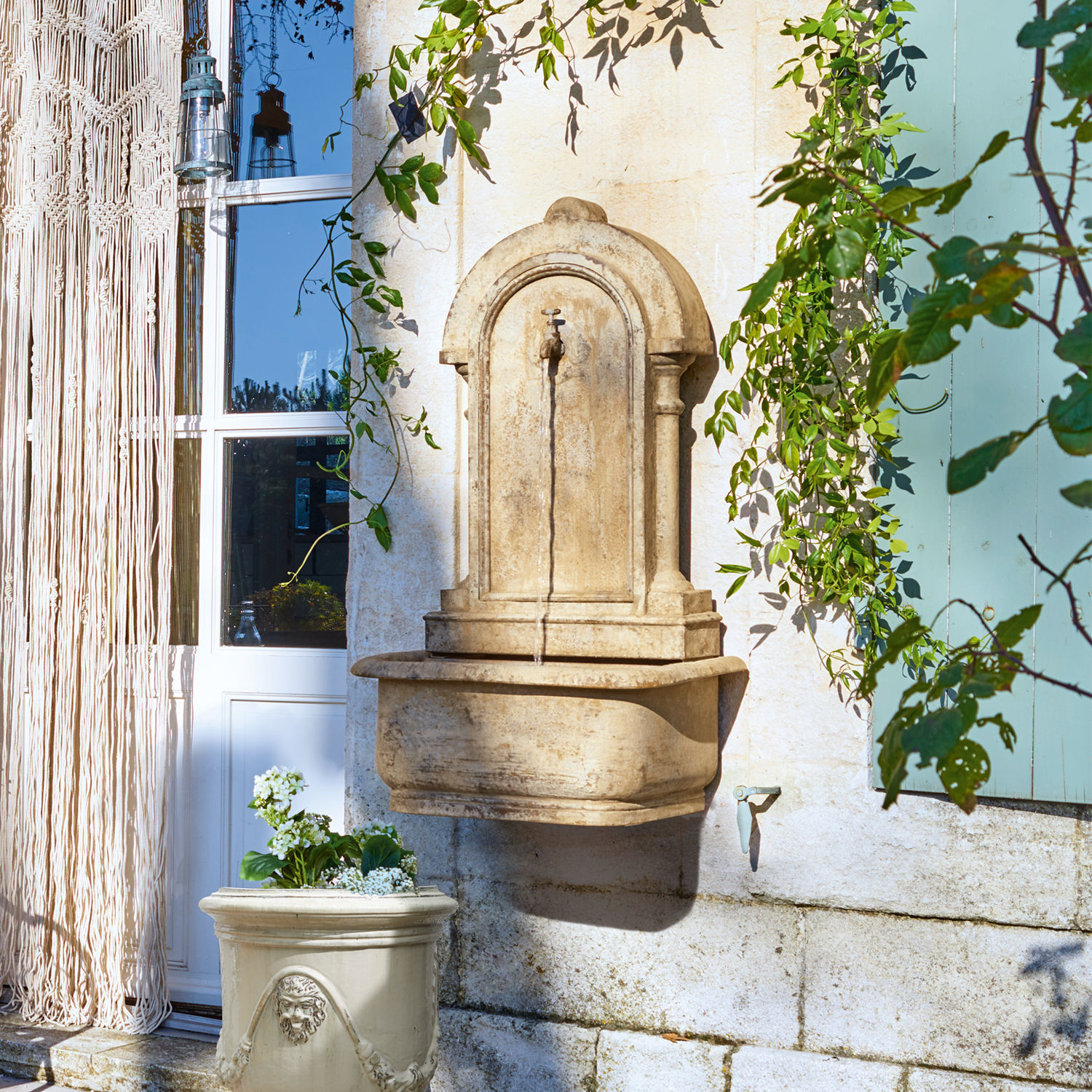 Kremefarbene Steinwandbrunnen mit Wasserhahn und Blumentopf vor einem Haus