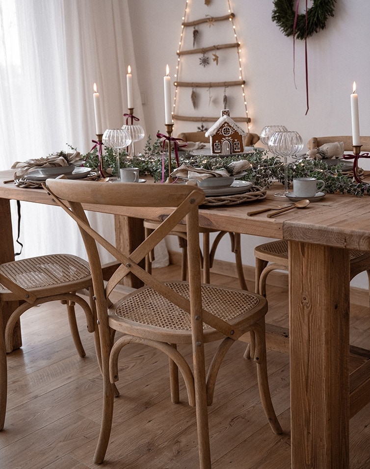 Holztisch mit Naturholzstühlen und Weihnachtsdeko mit Lebkuchenhaus und Kerzen