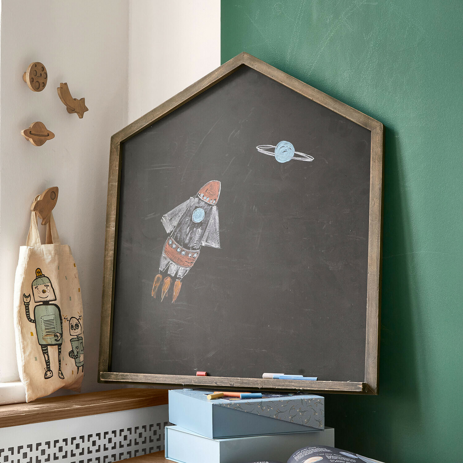 Hausförmige Kreidetafel mit Holzrahmen und Raketen- sowie Planetenzeichnung im Kinderzimmer