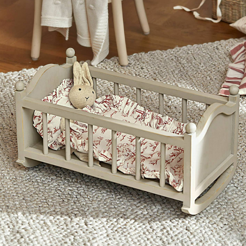 Graues Holzpuppenbett mit Plüschhase und gemusterter Bettwäsche auf Teppich