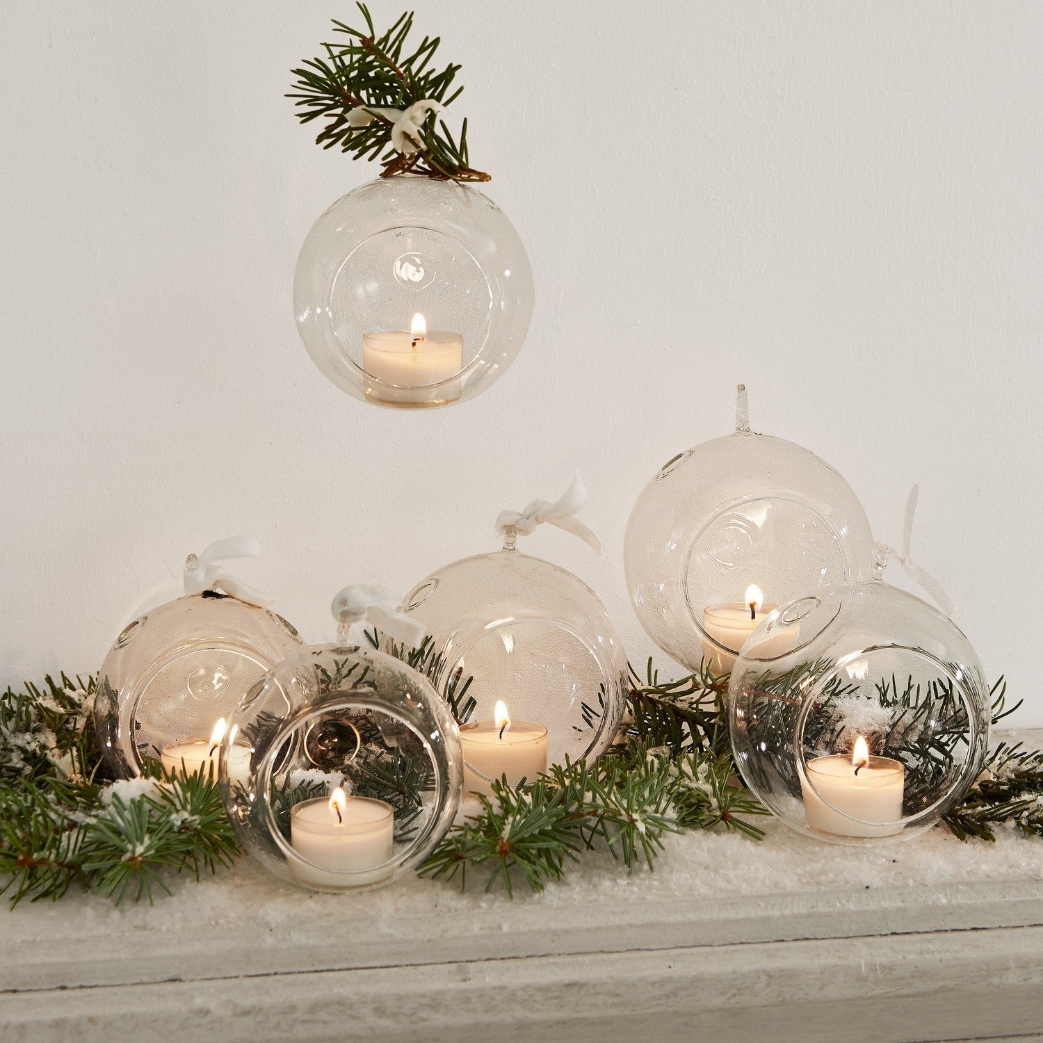 Glaskugeln als Kerzenhalter mit weißen Teelichtern und grünen Zweigen als Weihnachtsdeko
