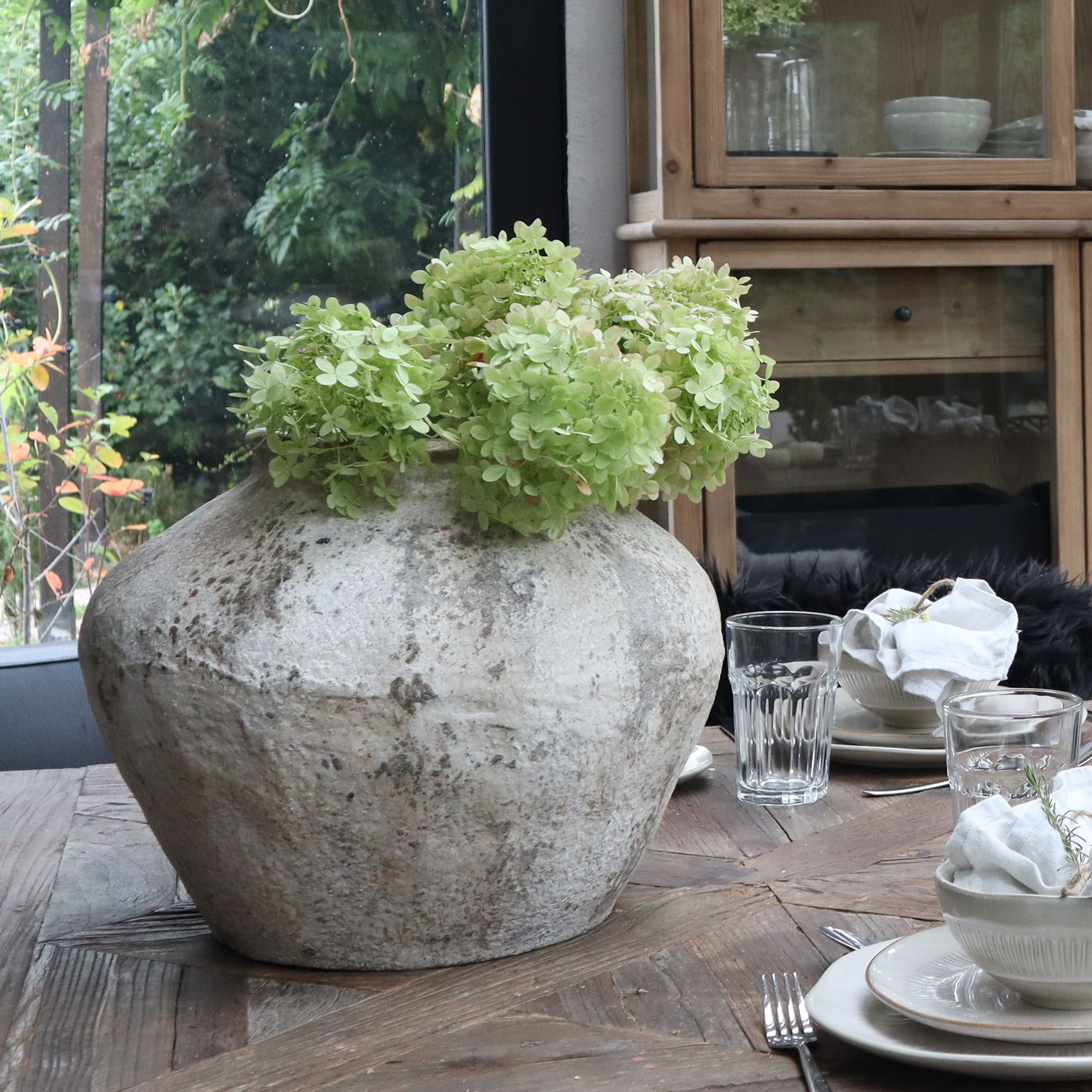 Große graue Keramikvase mit grünen Blumen auf Holztisch im Esszimmer