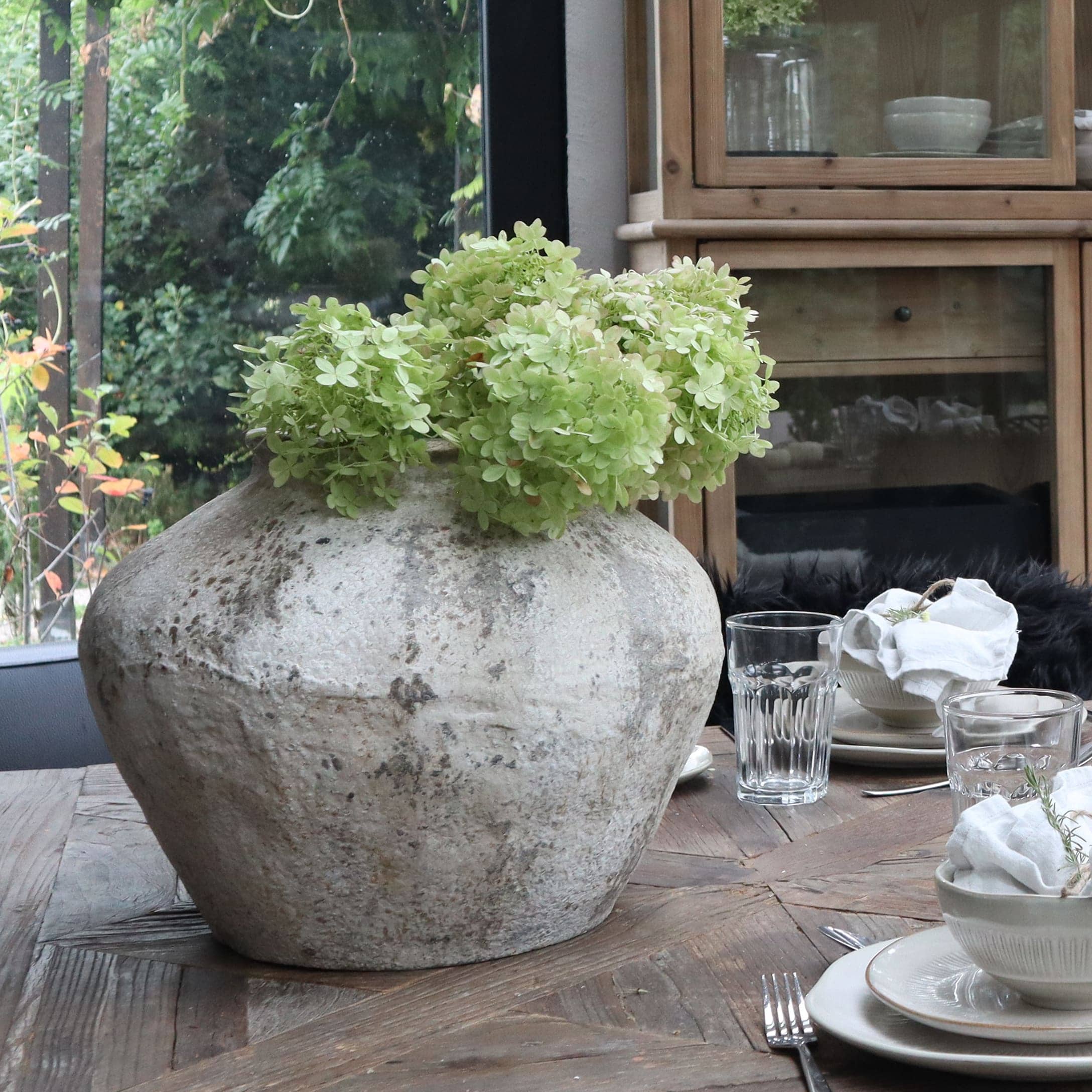 Große graue Keramikvase mit grünen Blumen auf Holztisch im Esszimmer
